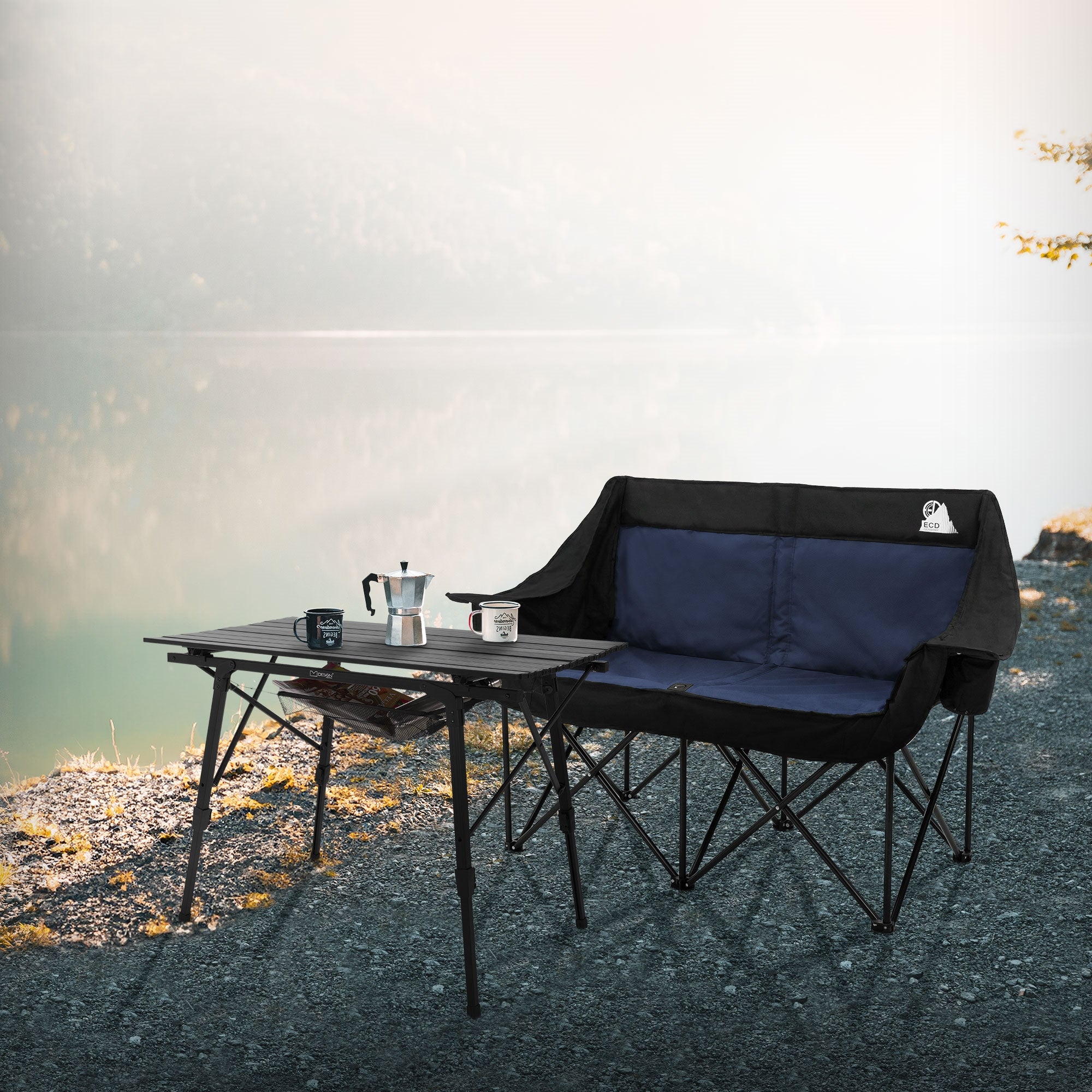 Schwarzes Campingsofa und Tisch am Ufer eines ruhigen Sees.