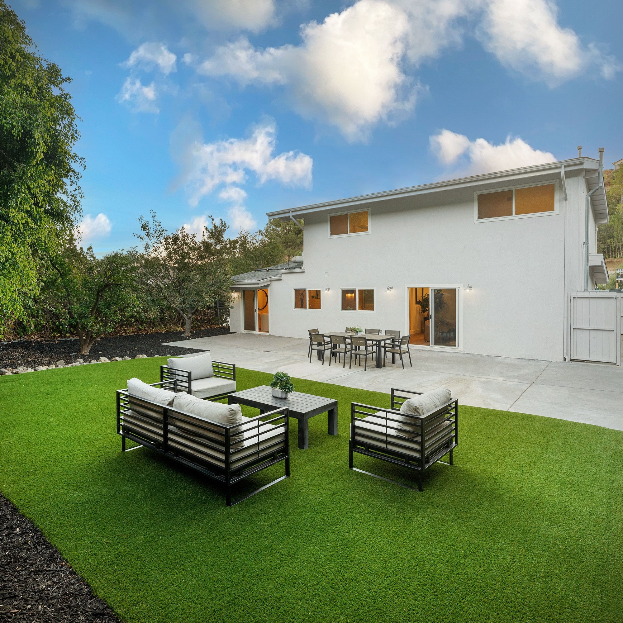 Have med grønt kunstgræs, havemøbler og et moderne hus i baggrunden.
