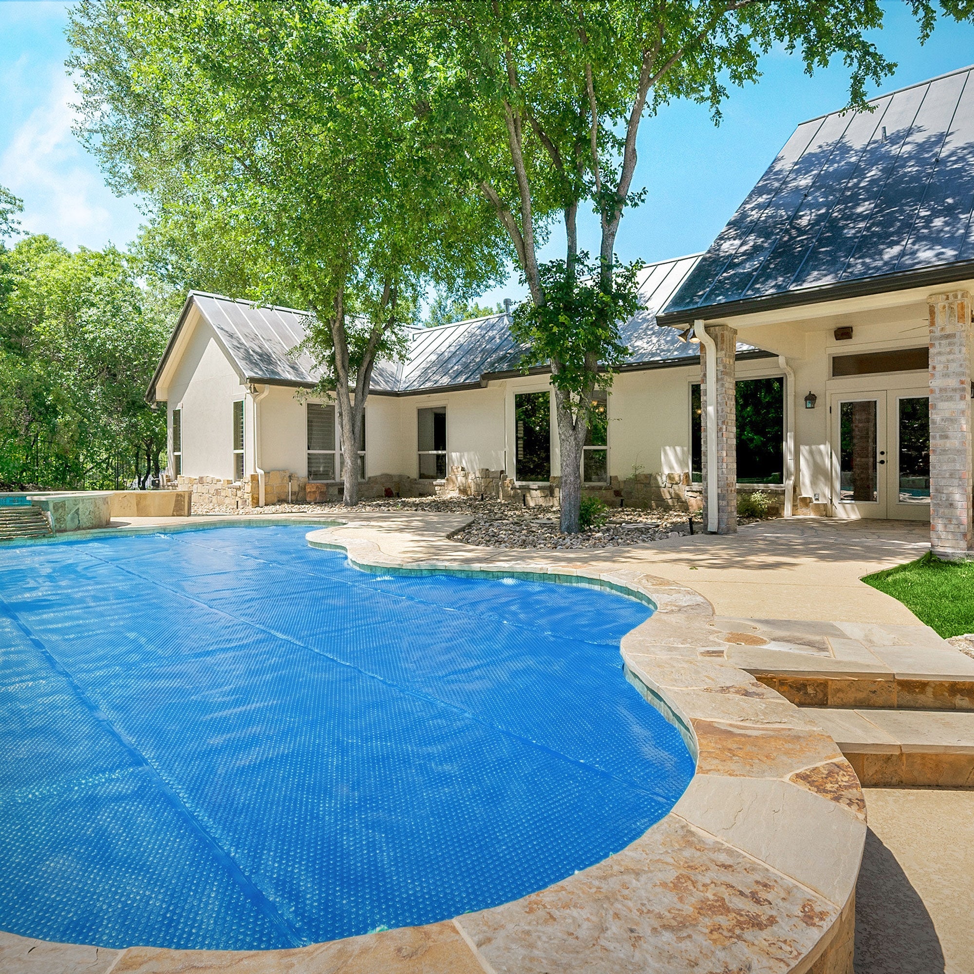 Pool mit blauer Abdeckung, umgeben von Bäumen und einem Haus.