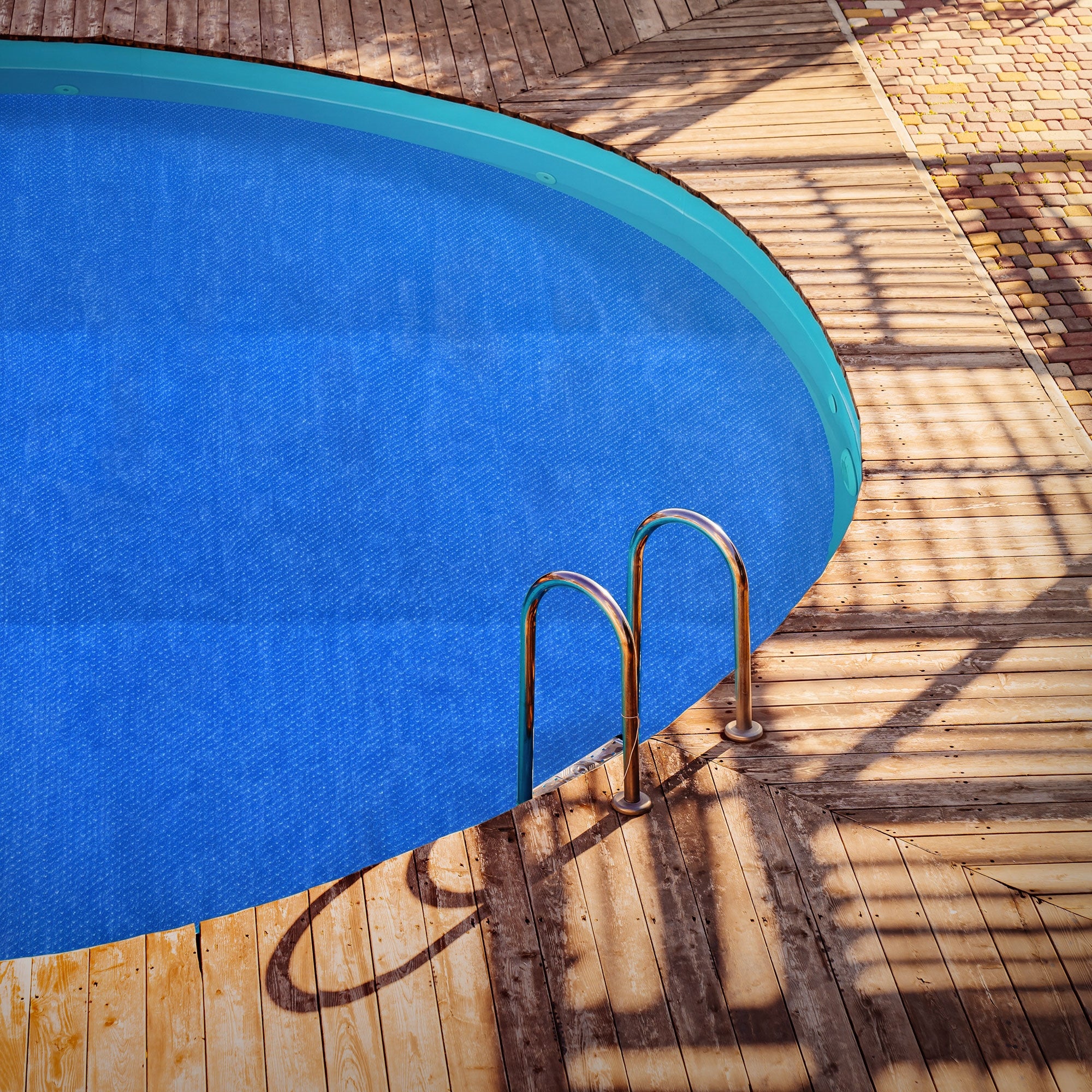 Blick auf einen runden Pool mit blauer Solarfolie und Holzumrandung.