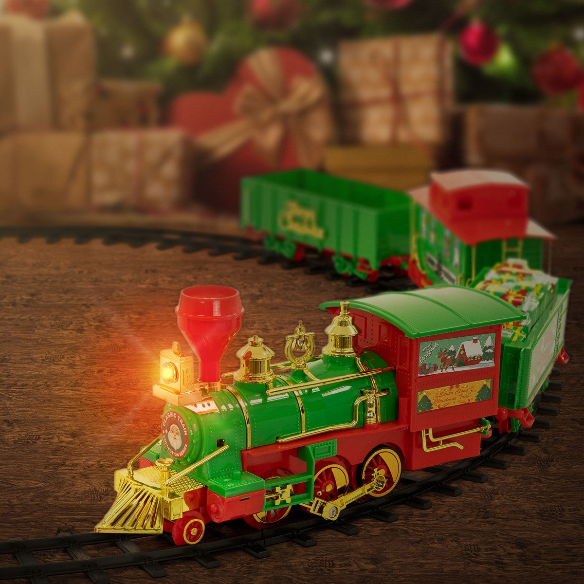 Grüne Spielzeugeisenbahn mit Lokomotive und Wagen auf Schienen vor Geschenken und Weihnachtsdekoration.