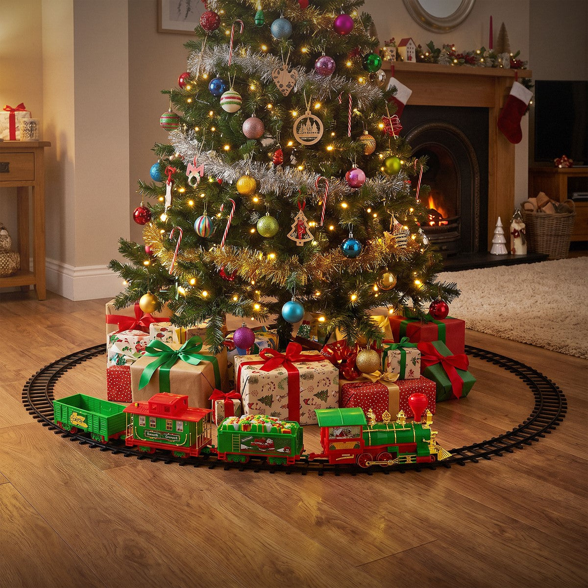 Grüner Weihnachtszug fährt auf einem Gleis um einen geschmückten Weihnachtsbaum mit Geschenken.