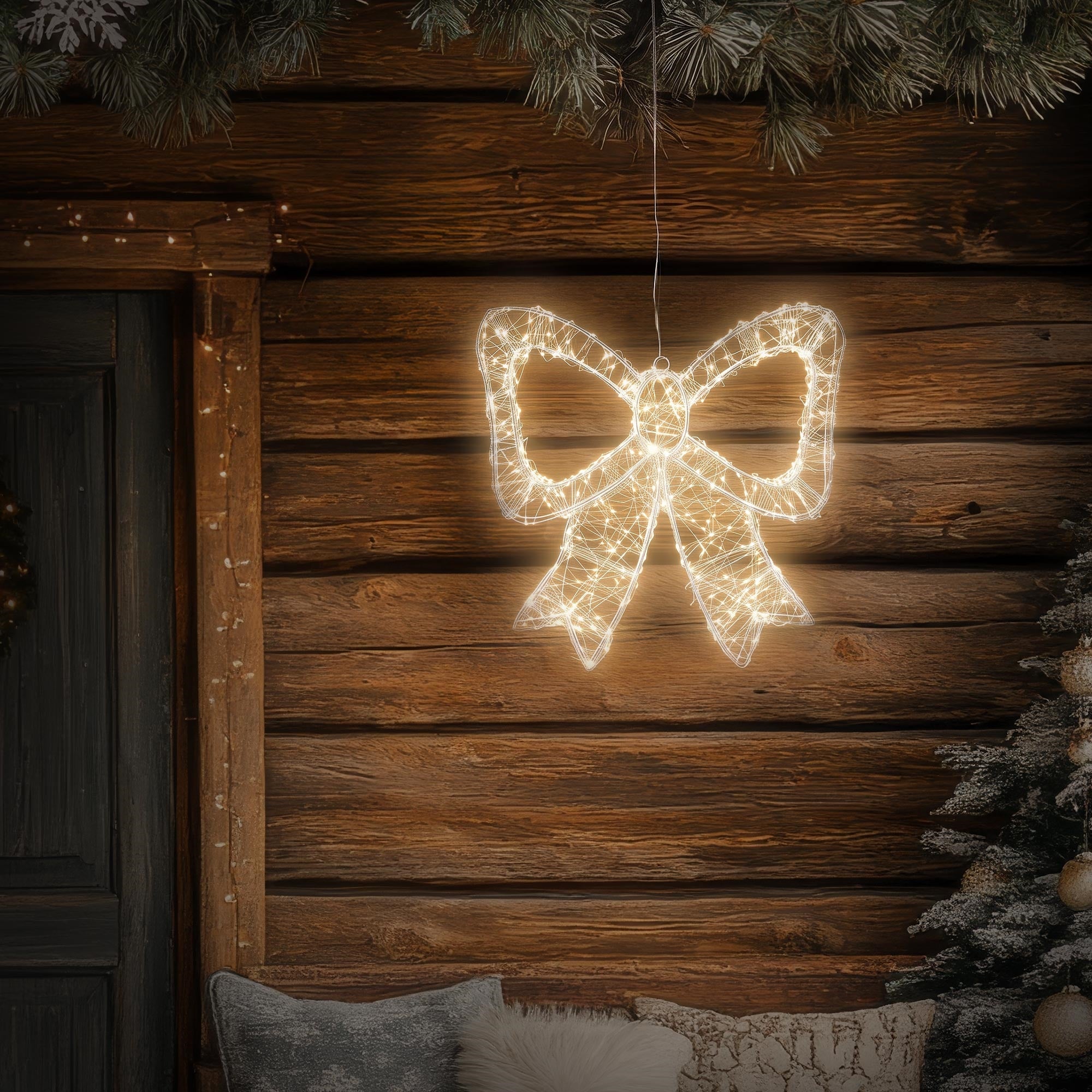 Illuminated bow hanging in front of a wooden panel and fir branches.