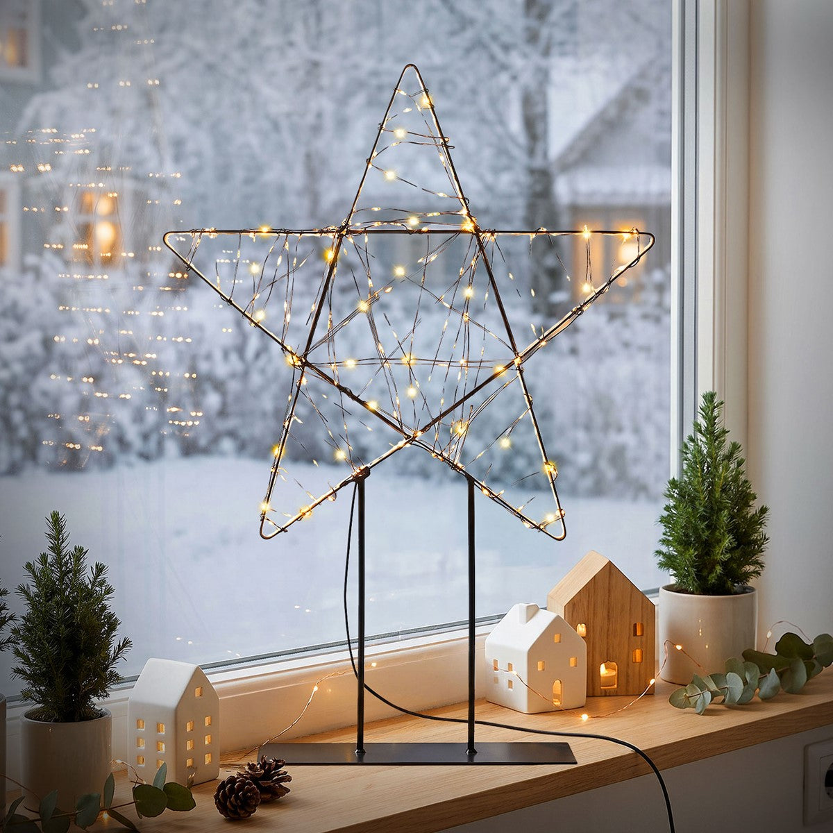 Étoile illuminée sur un rebord de fenêtre avec un paysage hivernal en arrière-plan.