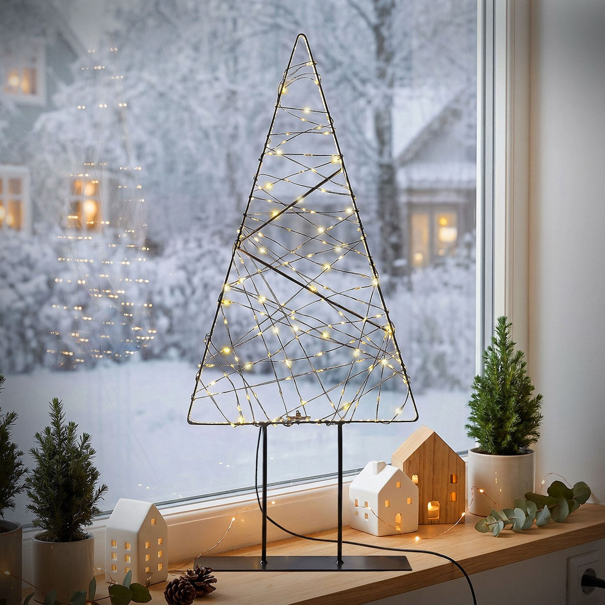 Arbre en fil de fer avec des lumières sur un rebord de fenêtre, avec un paysage enneigé en arrière-plan.