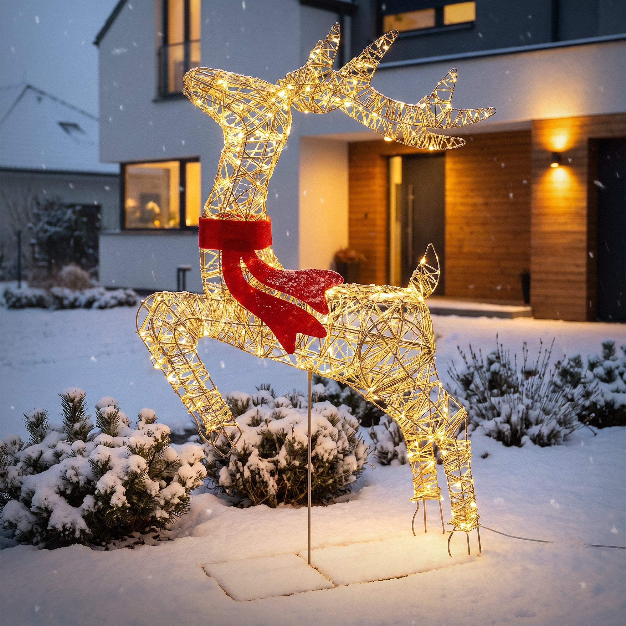 Leuchtendes Rentier im Schnee vor einem modernen Haus.