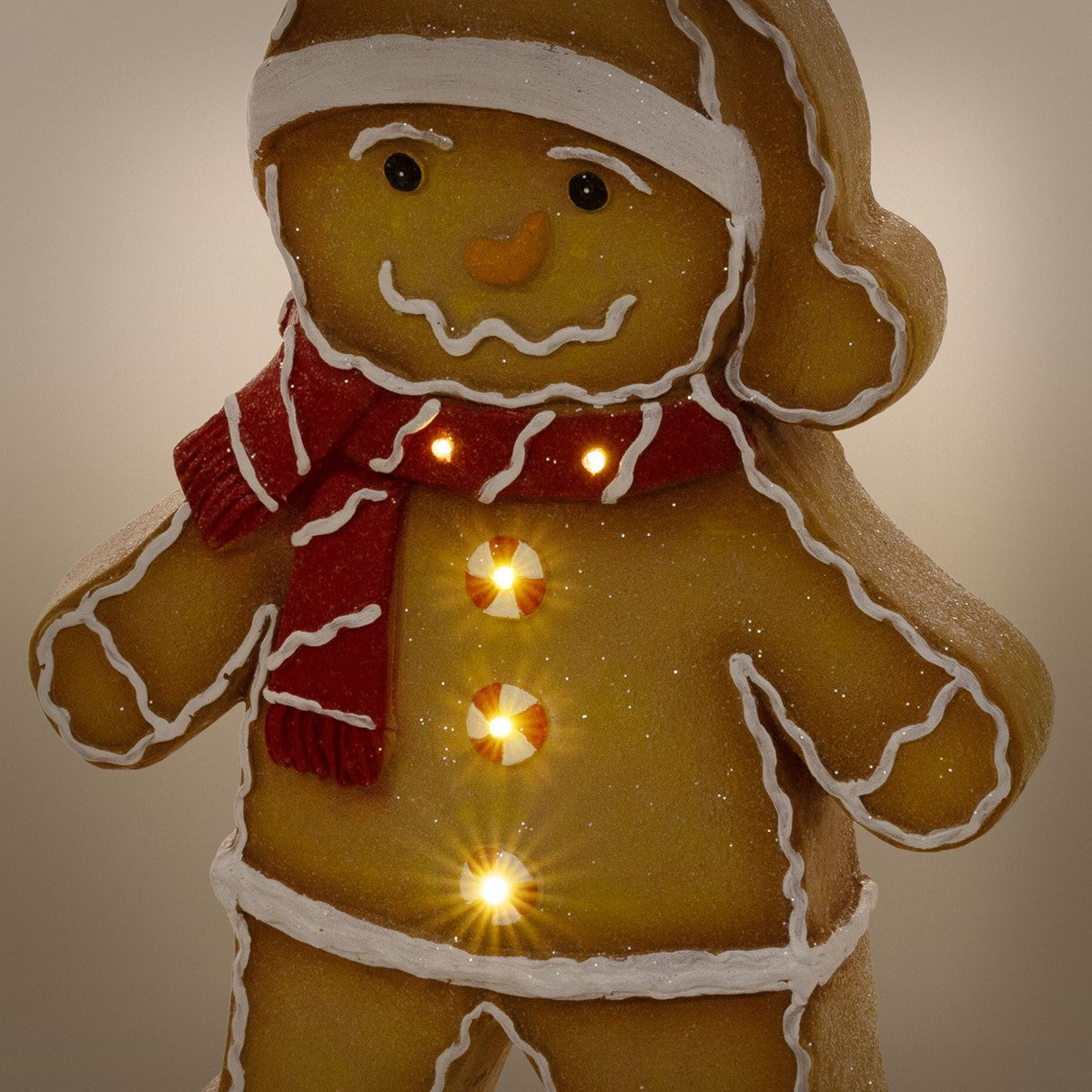 Lebkuchenfigur mit rotem Schal und leuchtenden Knöpfen, vor neutralem Hintergrund.