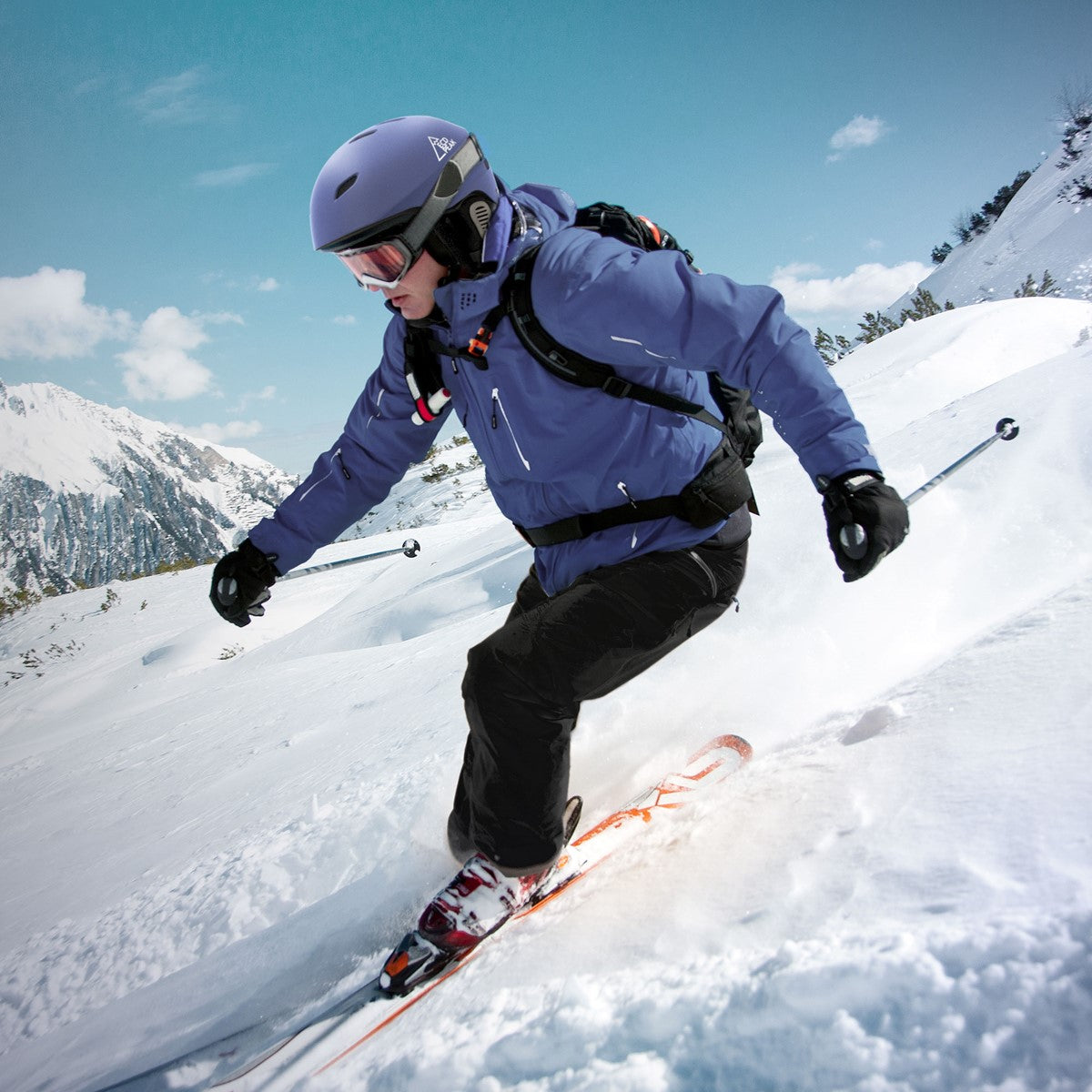 Skifahrer in blauer Jacke und Helm fährt durch den Schnee in den Bergen.