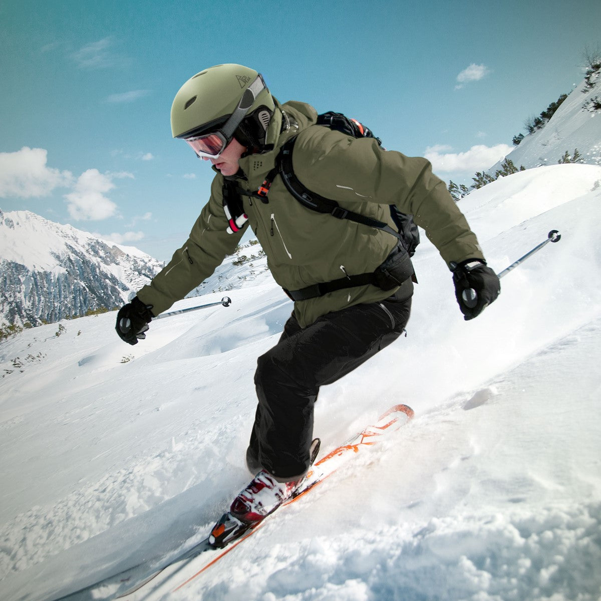 Skifahrer in grünem Anzug fährt durch den Schnee mit Bergen im Hintergrund.