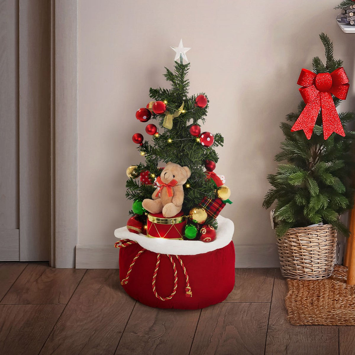 Kleiner Weihnachtsbaum mit Spielzeugbär und roten Ornamenten auf einem roten Sockel.