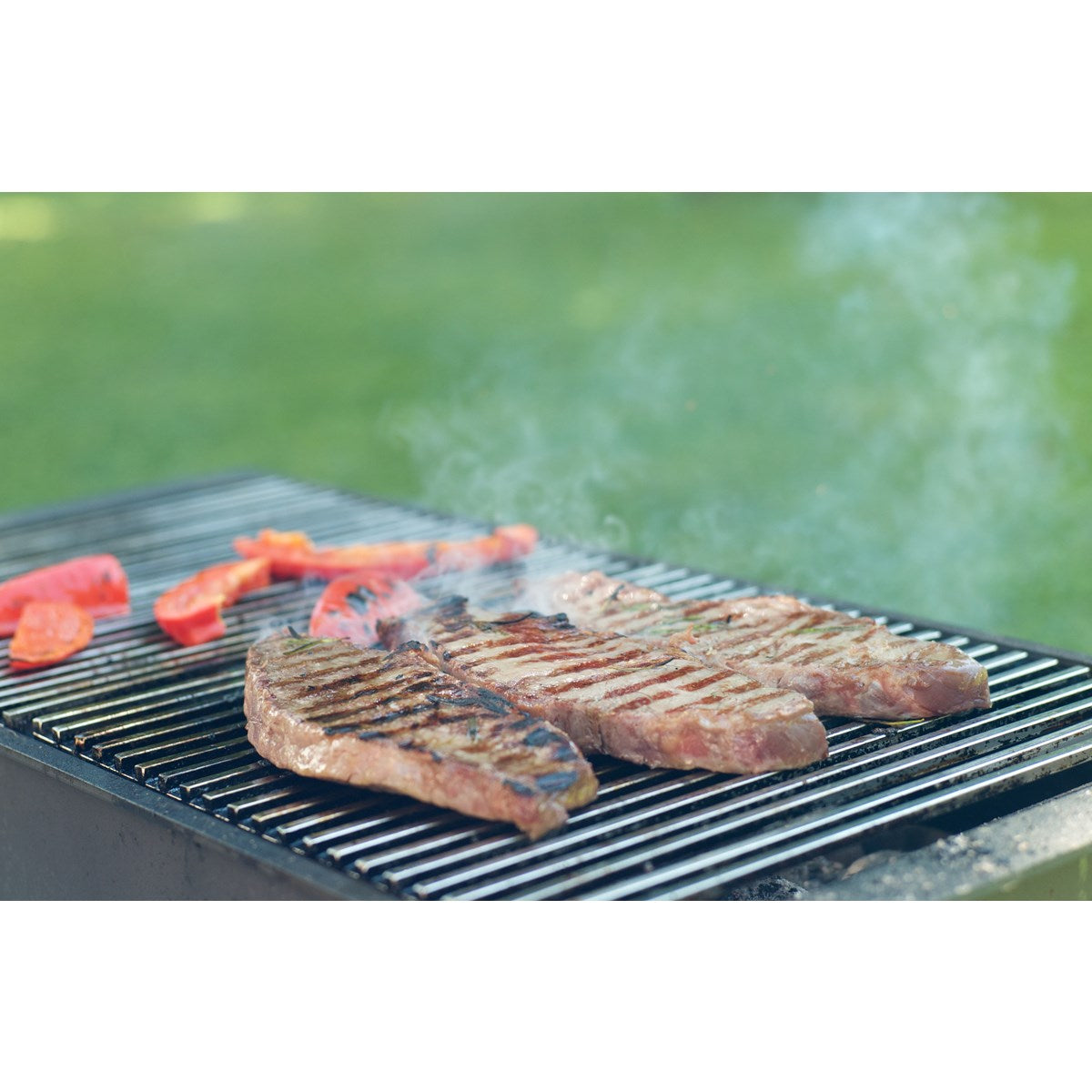 Drei gegrillte Steaks mit Gemüse auf einem Grill im Freien.