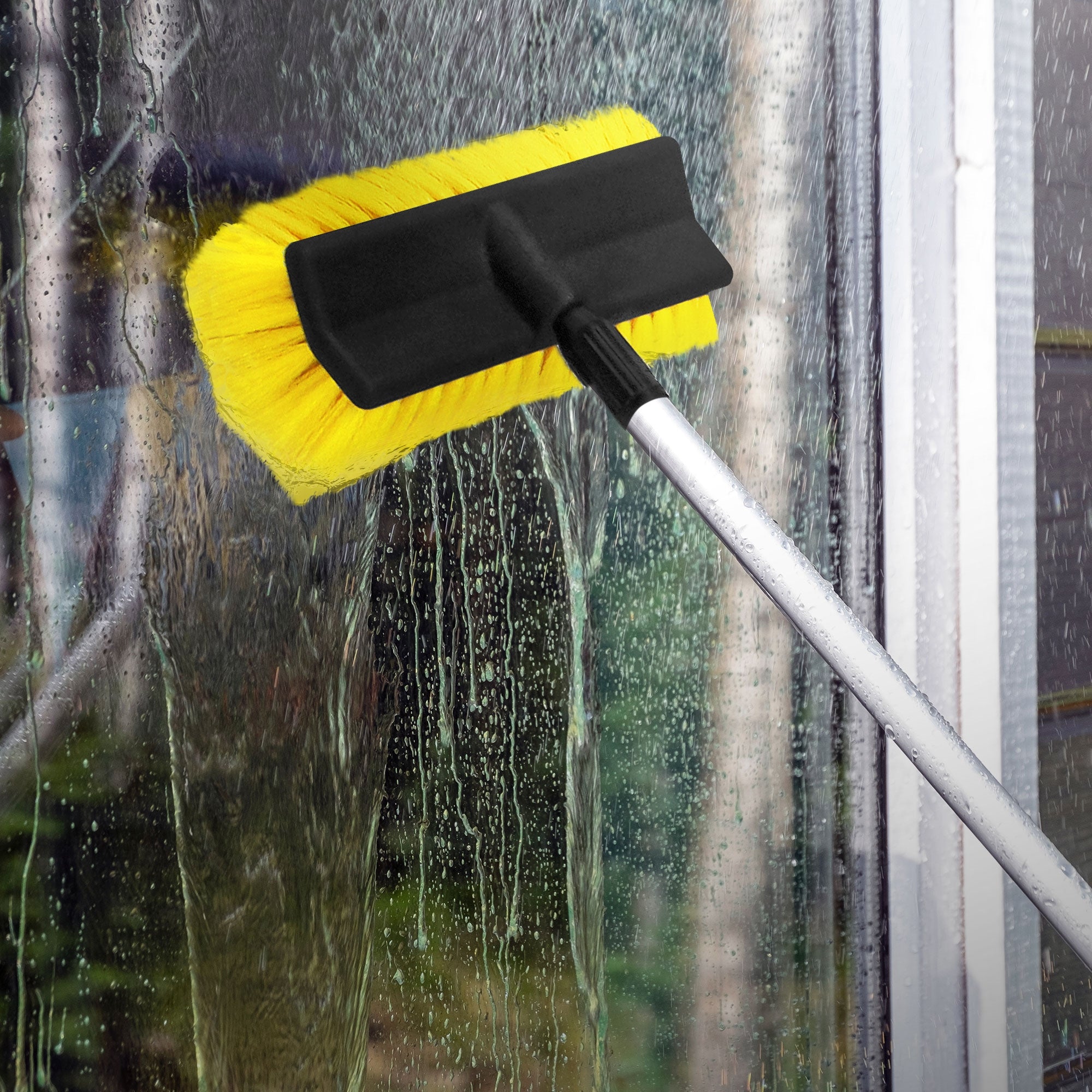 Gelbe Reinigungsbürste wird an einem Fenster verwendet, Wasser läuft herunter.