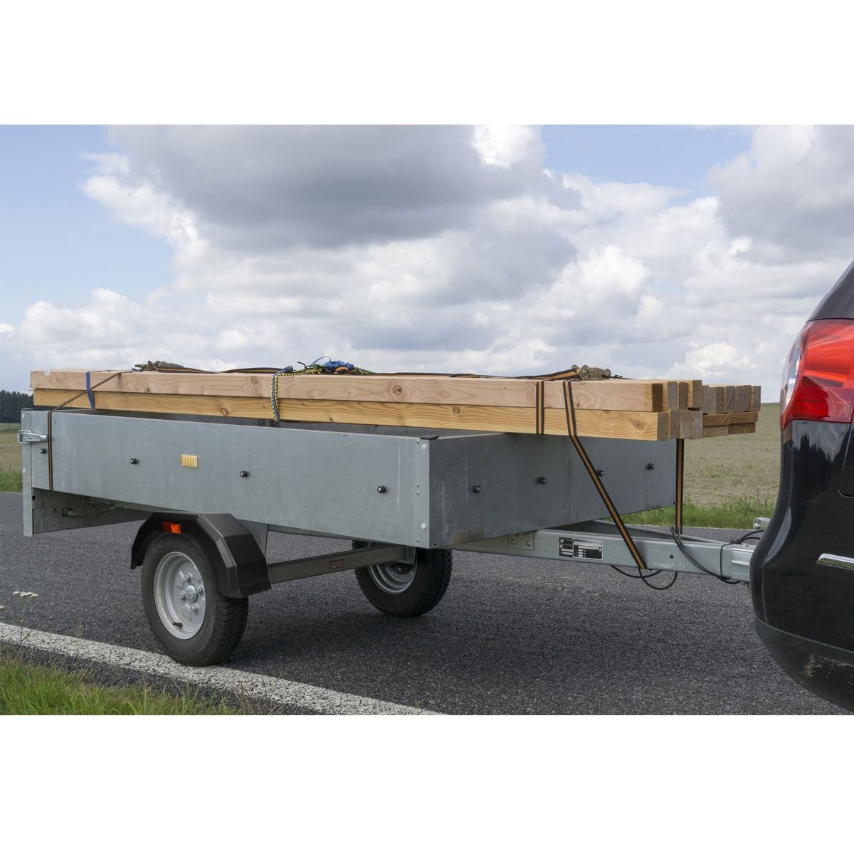 Anhänger mit Holzlatten, auf einer Straße, Wolken am Himmel.