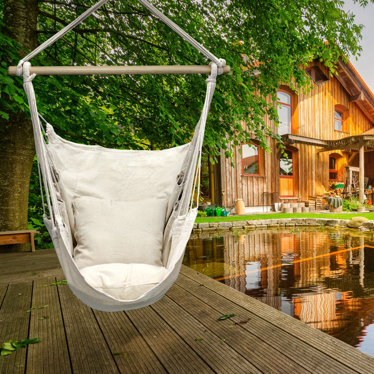 Hängesessel aus hellem Stoff, vor einem Holzhaus am Wasser.