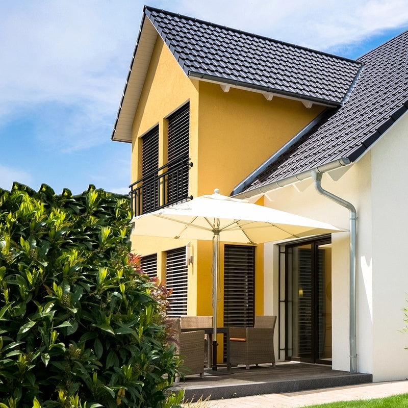 Casa con facciata gialla, terrazza e ombrellone, circondata da piante.