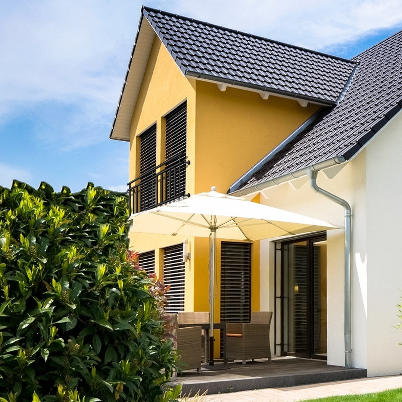 Haus mit gelber Fassade, Balkon und Sonnenschirm im Garten.
