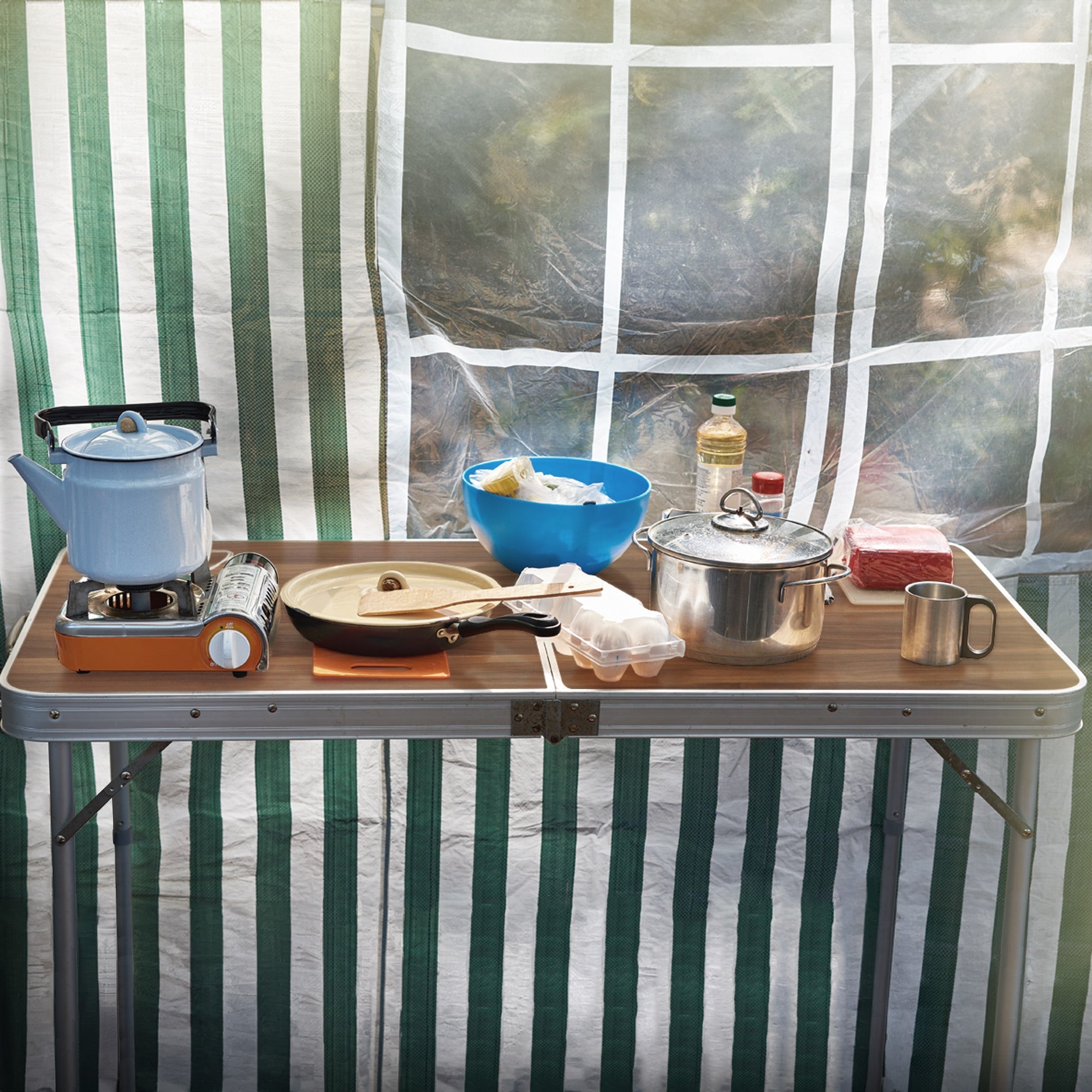Una mesa con utensilios de cocina, ollas y alimentos, frente a una tienda.