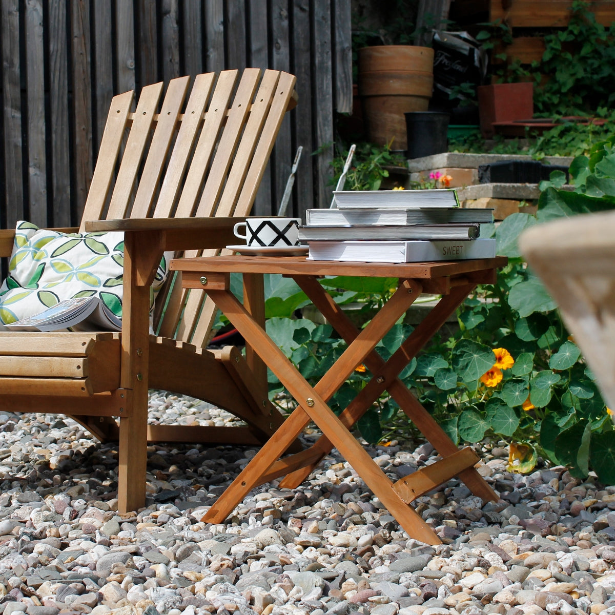 Transat en bois avec table d'appoint et livres dans le jardin.