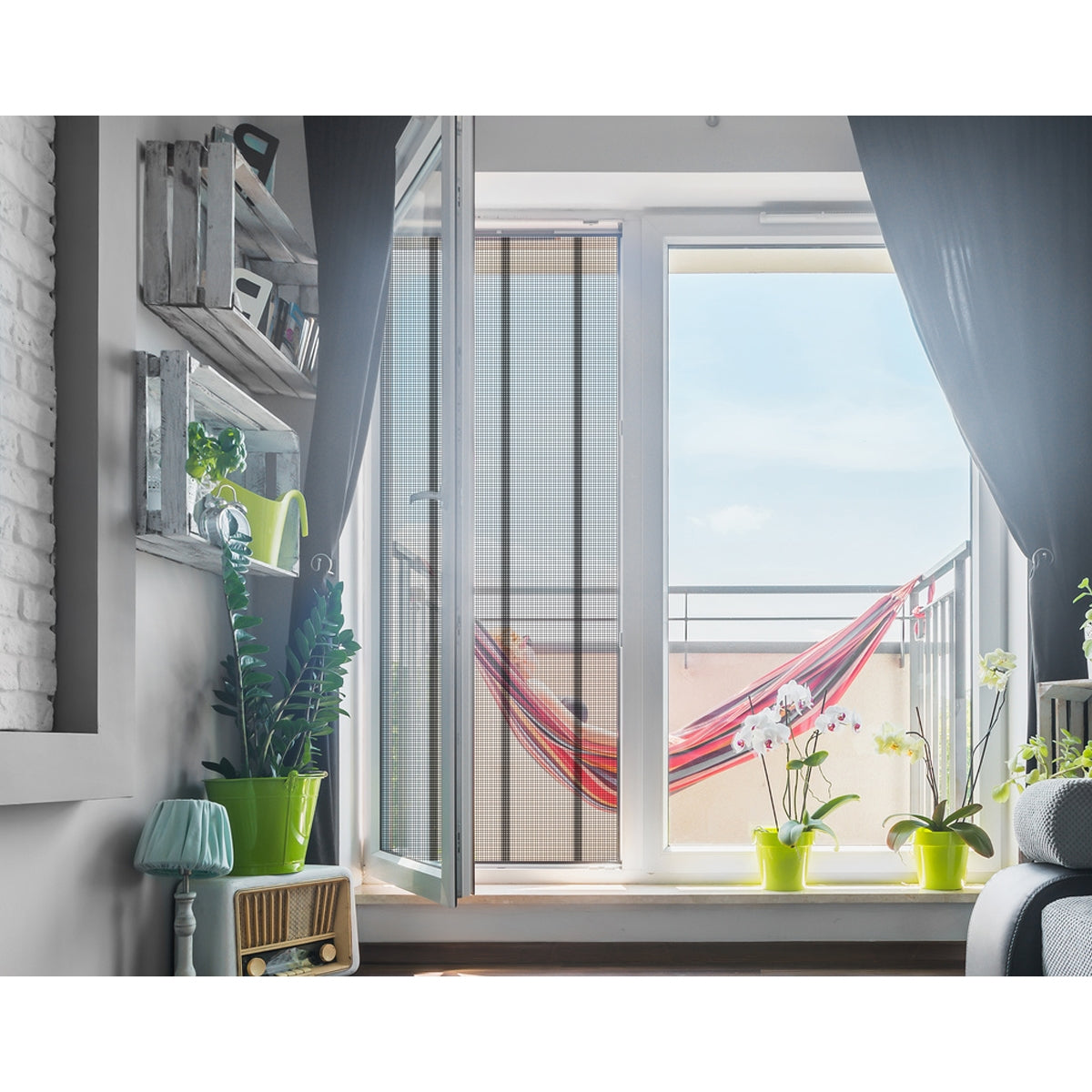 Blick auf einen Balkon mit einer Hängematte und Pflanzen vor einem offenen Fenster.
