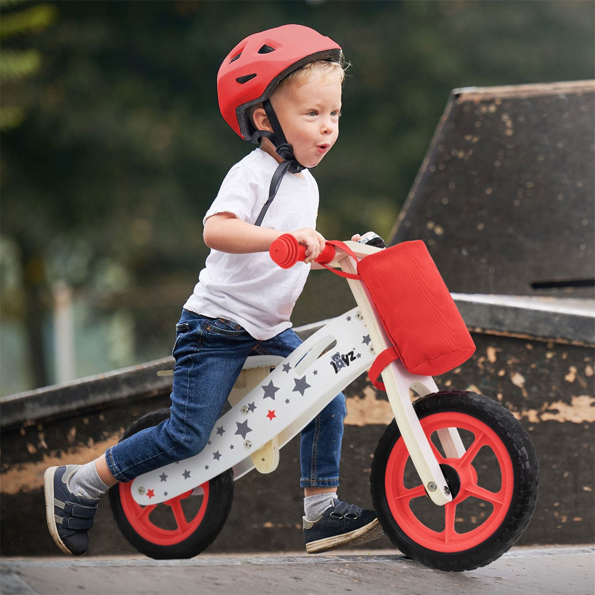 A child is riding a balance bike and wearing a red helmet.