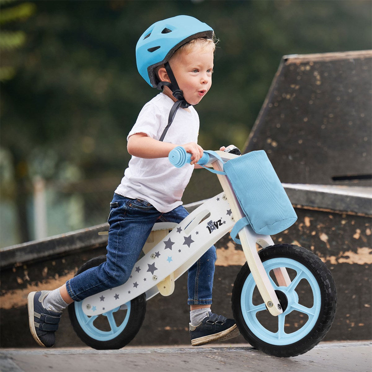 A boy rides a balance bike down a ramp while wearing a helmet.