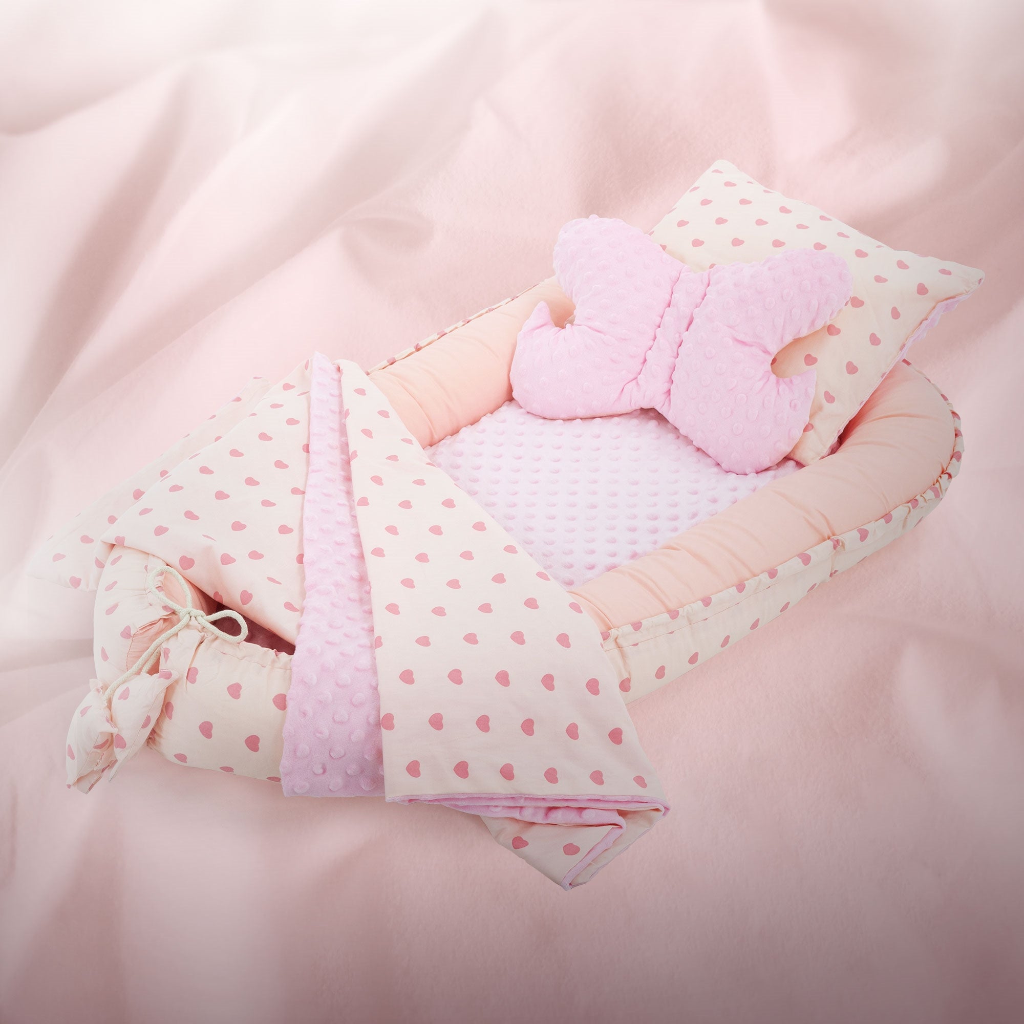 Nid rose avec motif de cœurs, coussin et couverture sur fond rose.