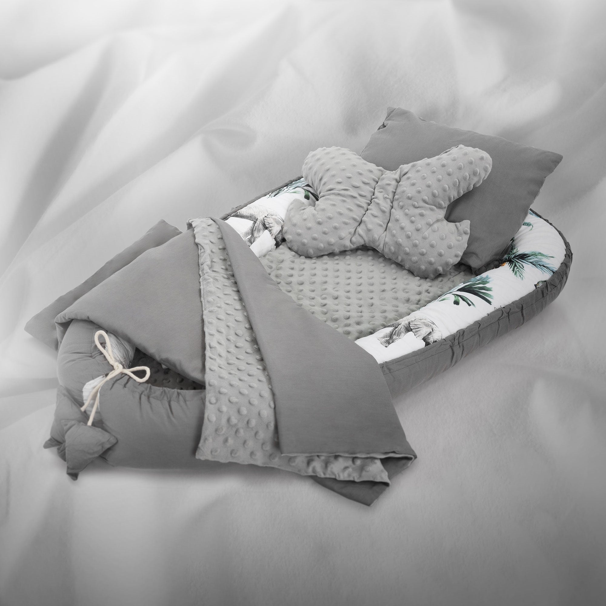 Ein graues Babybett mit einem Schmetterlingskissen und einer Decke mit Palmenmuster.