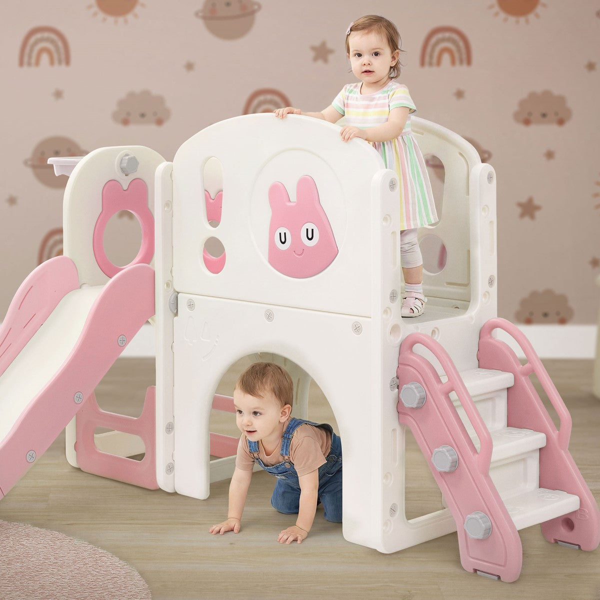 Two children playing on a play tower with a slide and a climbing element.