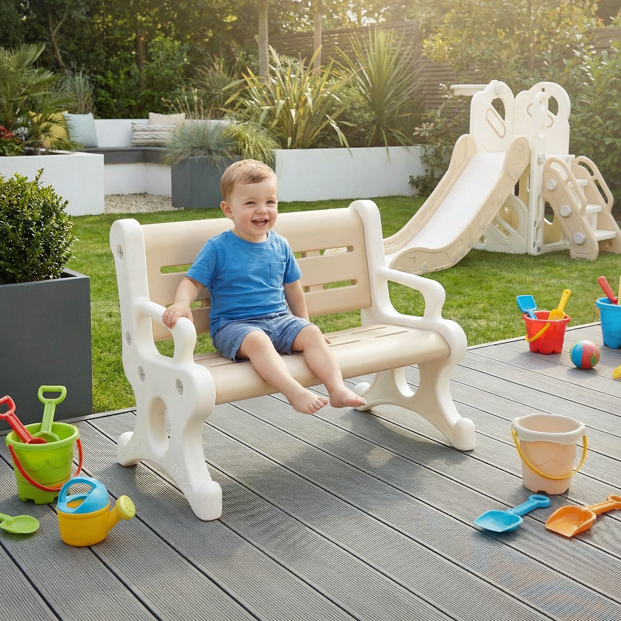 Ein Junge sitzt lächelnd auf einer weißen Bank, umgeben von Spielzeug im Garten.