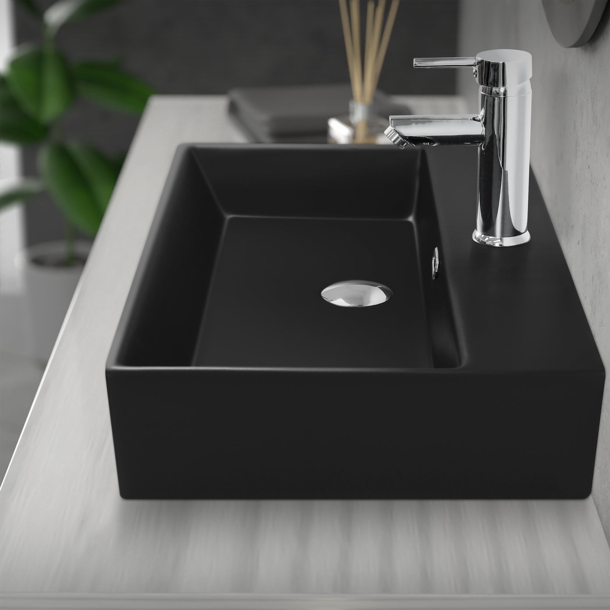 Schwarzes Waschbecken auf einem Tisch, Wasserhahn und Abfluss sichtbar.