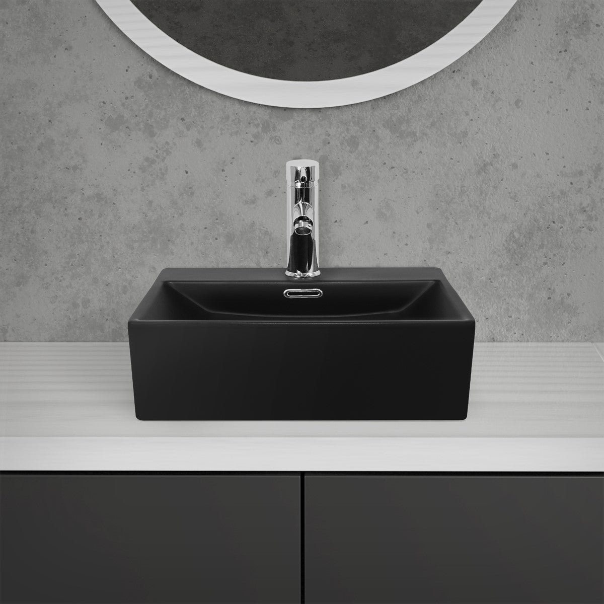 Black washbasin with a faucet in front of a grey wall.