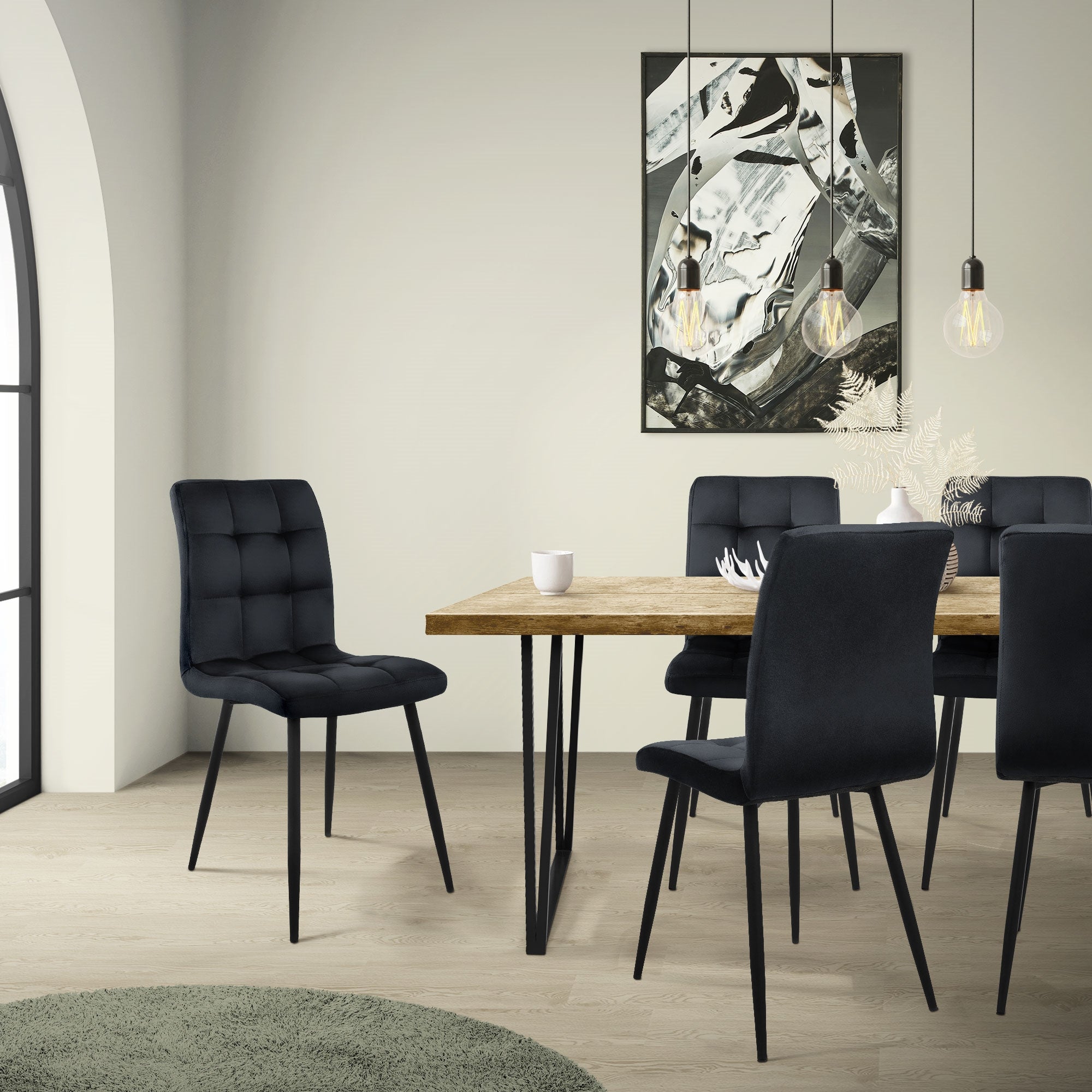 Ein Esszimmer mit einem Holztisch und schwarzen Stühlen, beleuchtet von hängenden Lampen.