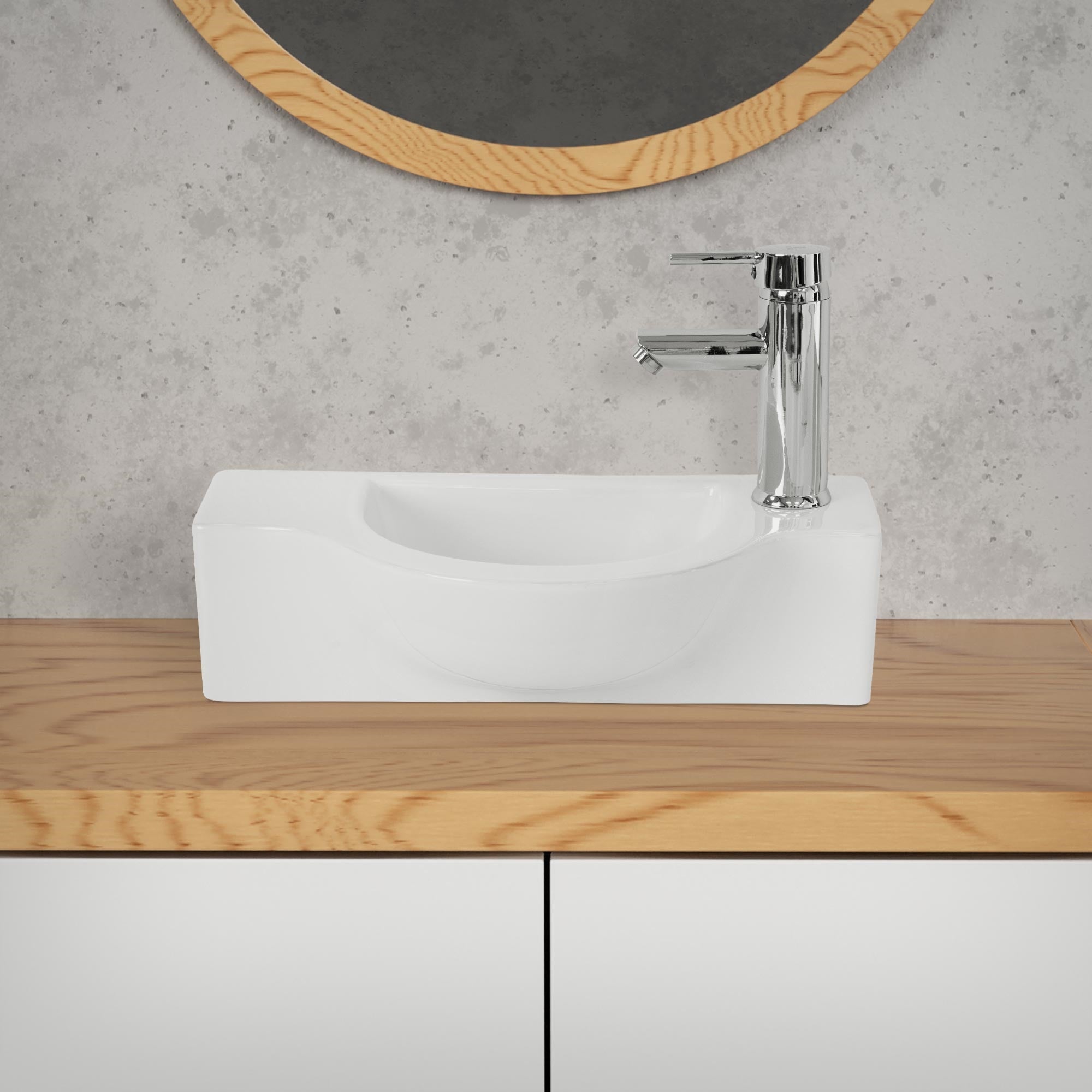 Weißes Waschbecken mit Wasserhahn und runder Spiegelfläche im Hintergrund.