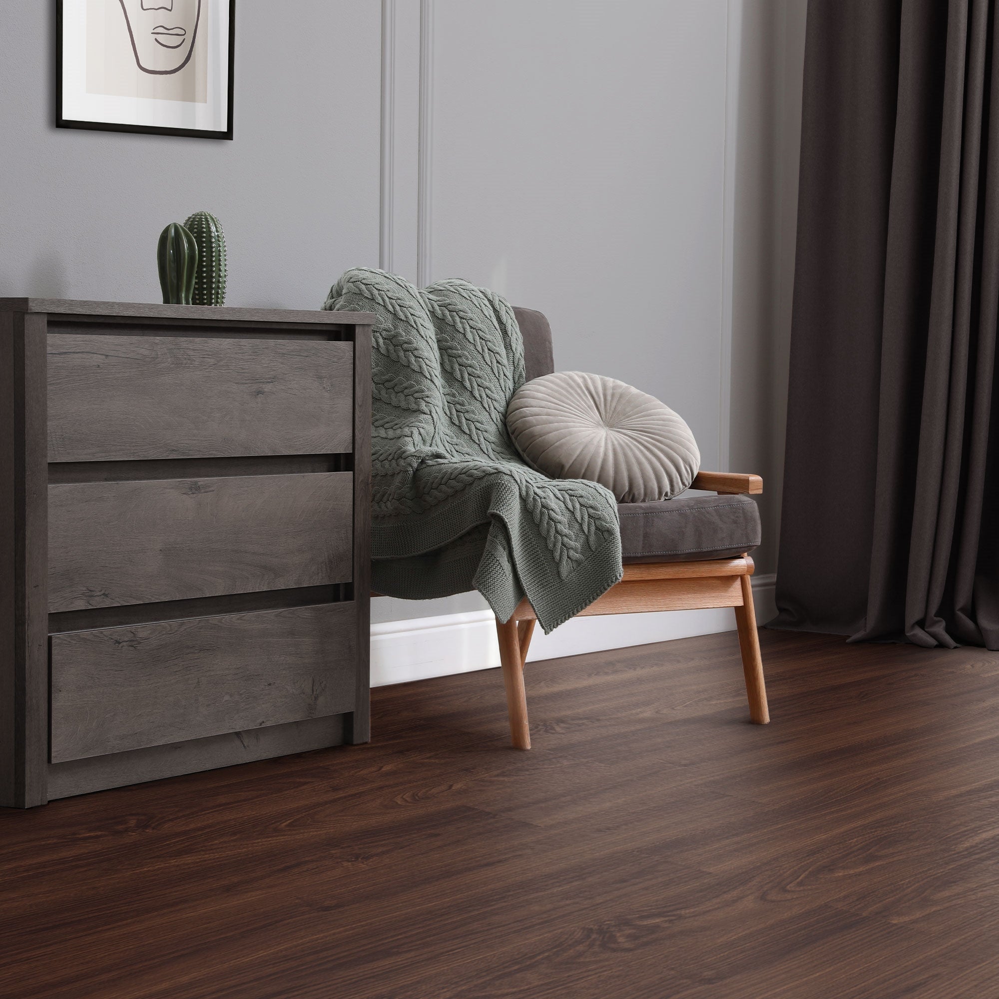 Sofa with blanket and cushions next to a dresser in a room.