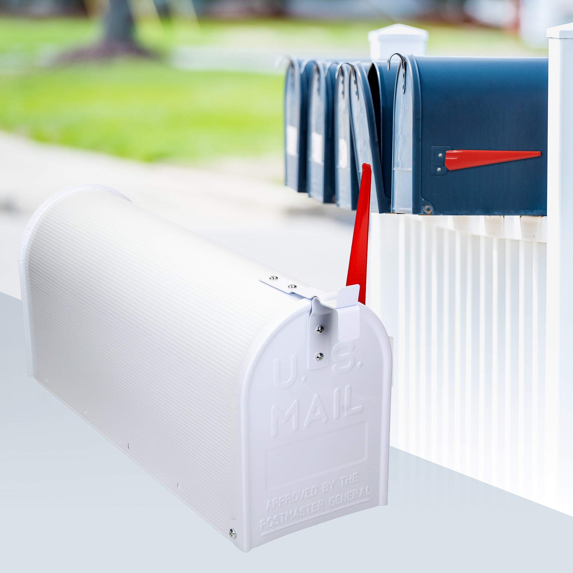 Weißer Briefkasten mit rotem Fahnenzeichen und mehreren Briefkästen im Hintergrund.
