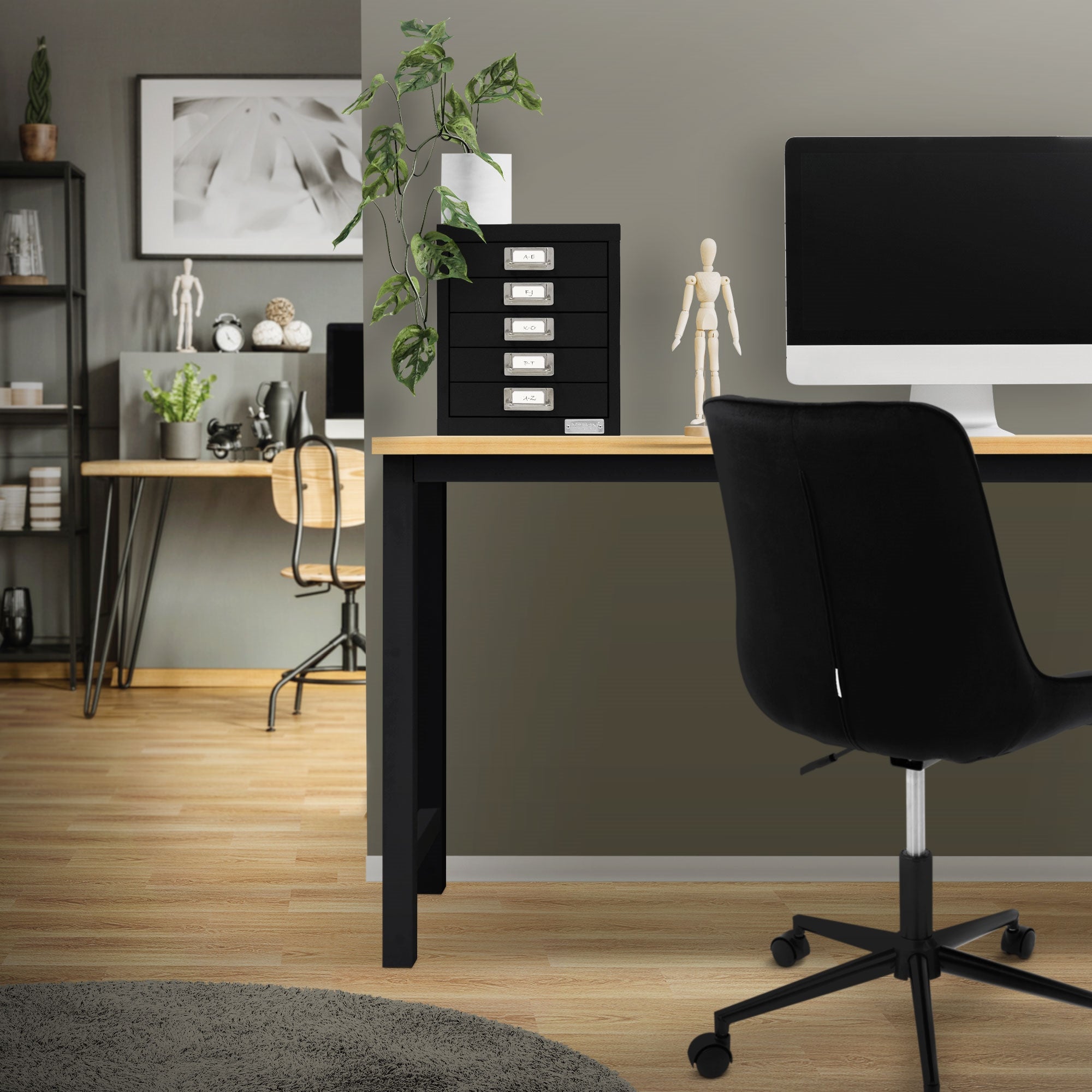 Büro mit schwarzem Aktenschrank, Computer und Pflanze auf dem Tisch.