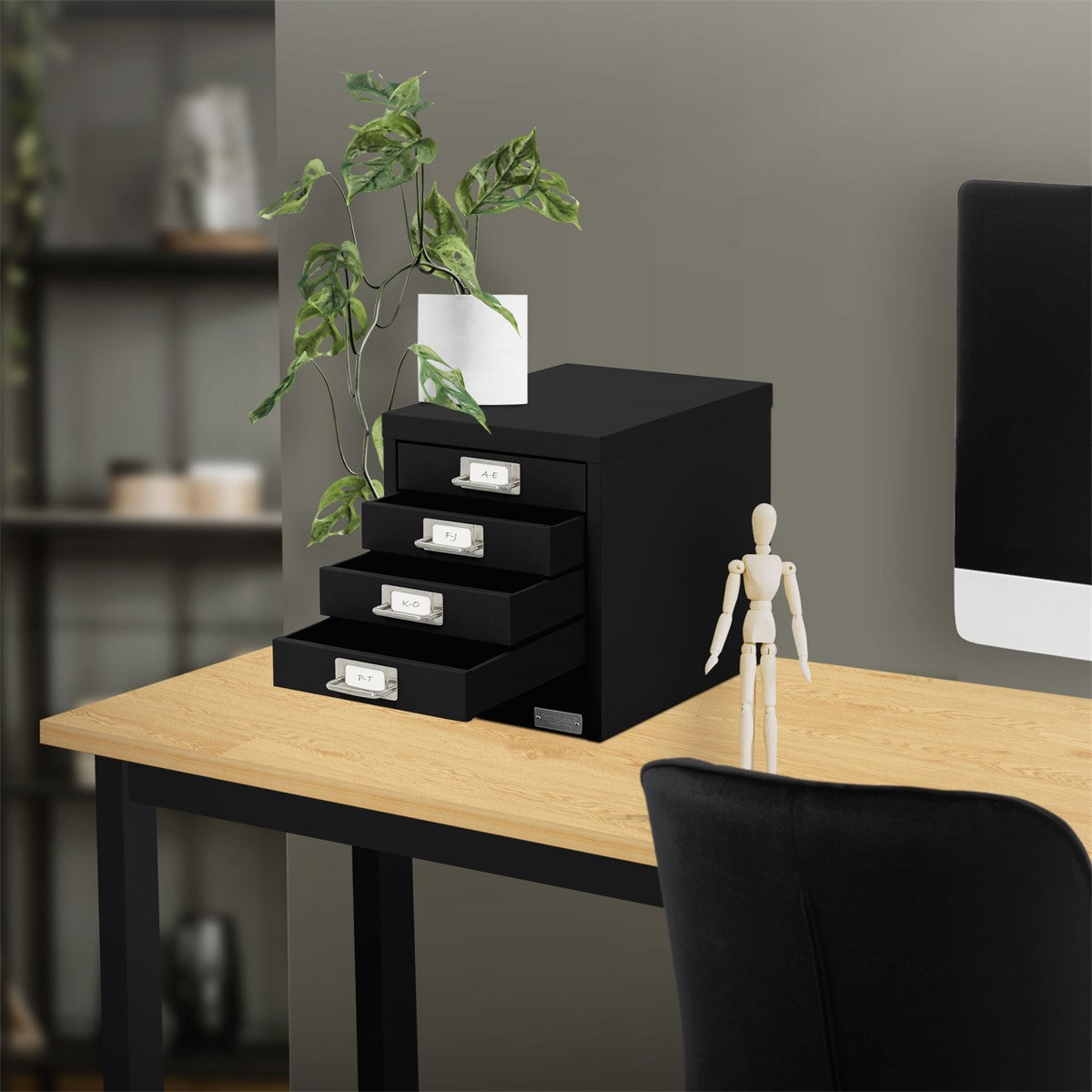 Schreibtisch mit schwarzem Schubladenschrank, Pflanze und Figur.