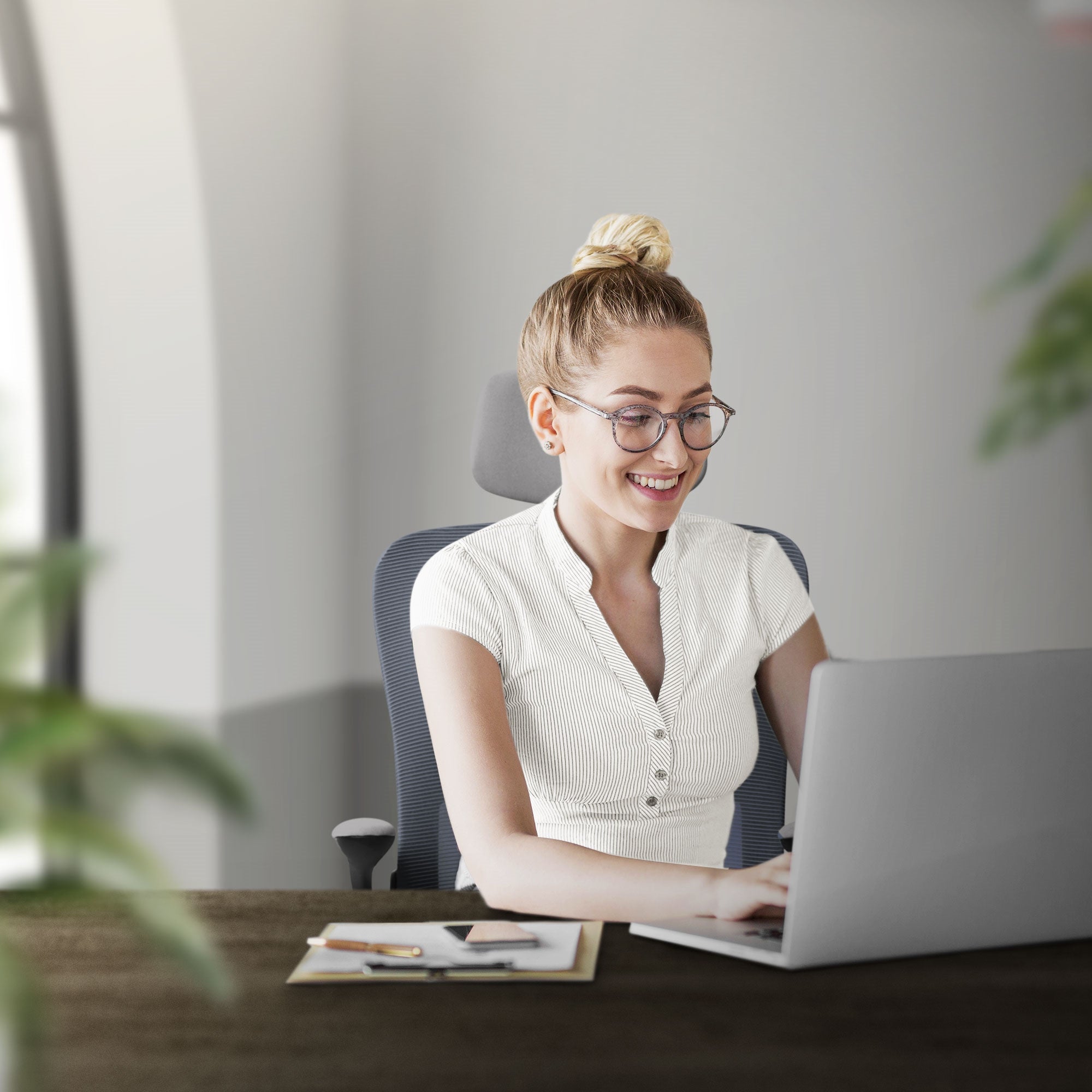 Junge Frau sitzt am Schreibtisch und arbeitet am Laptop, lächelt.
