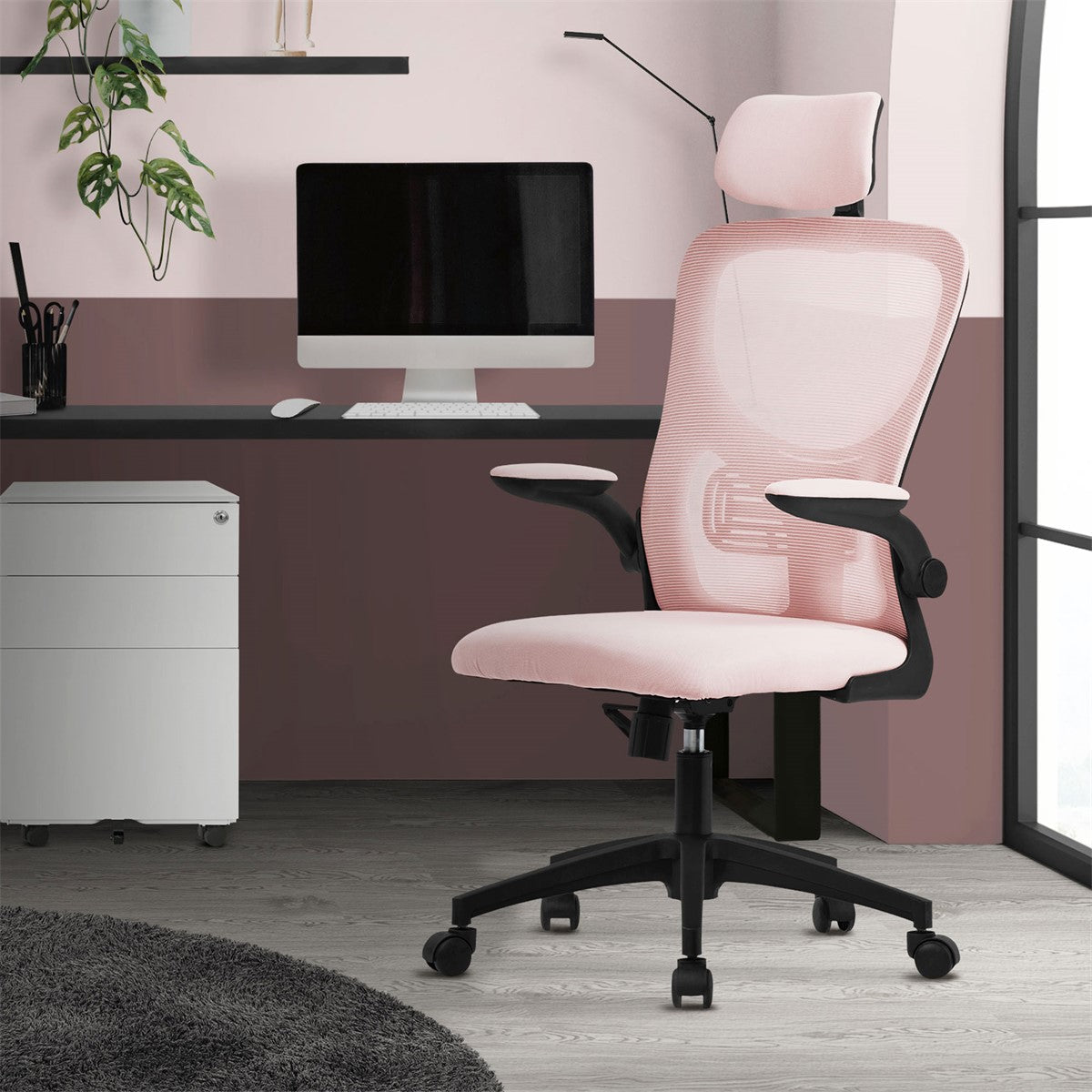 A pink office chair in front of a desk, with a computer and plants in the background.