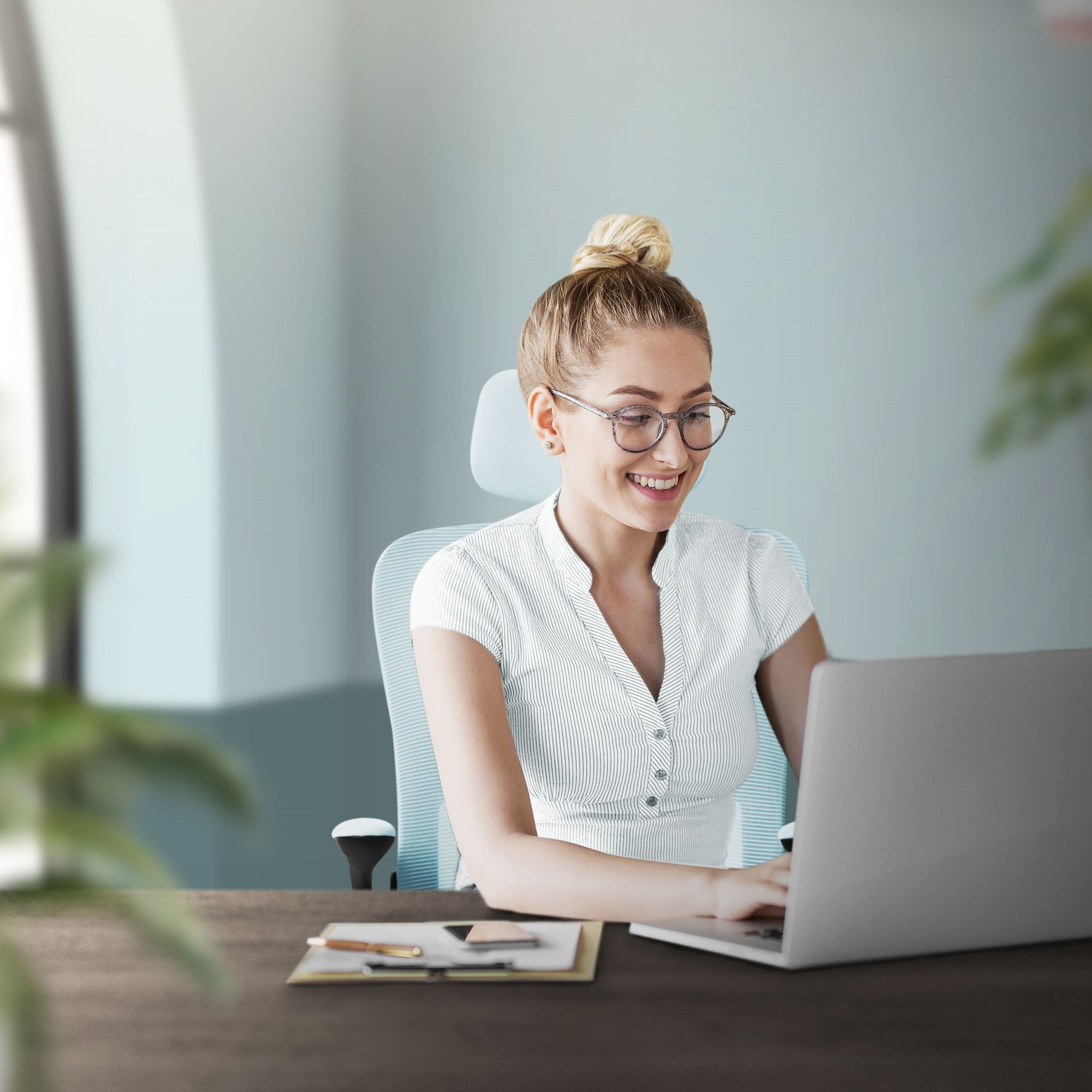 Lächelnde Frau am Laptop in einem modernen Büro mit Pflanzen im Hintergrund.