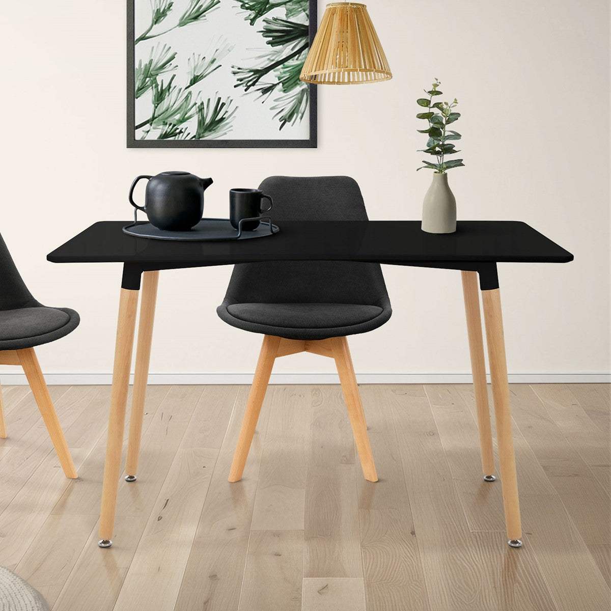 A black table with wooden legs, a teapot and a chair in a bright room.