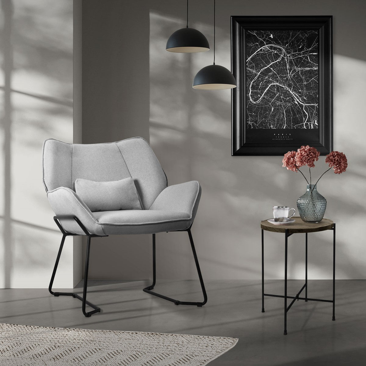 Ein grauer Sessel in einem Raum mit einem Bild und einer Blumenvase auf einem Tisch.