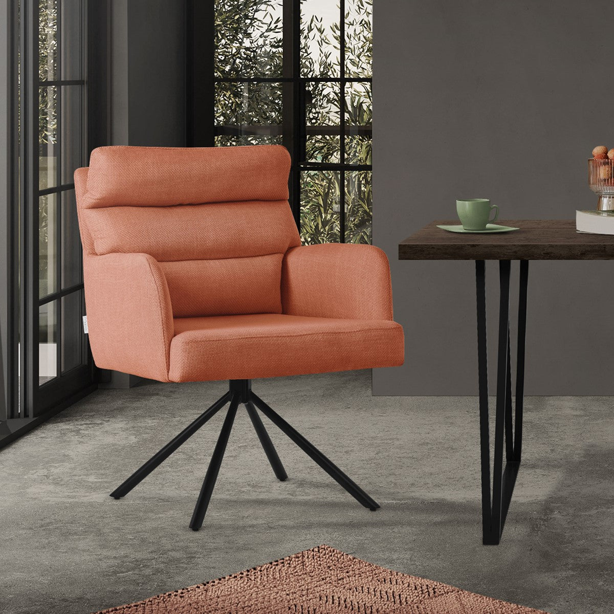 An orange armchair stands next to a table in a room with large windows