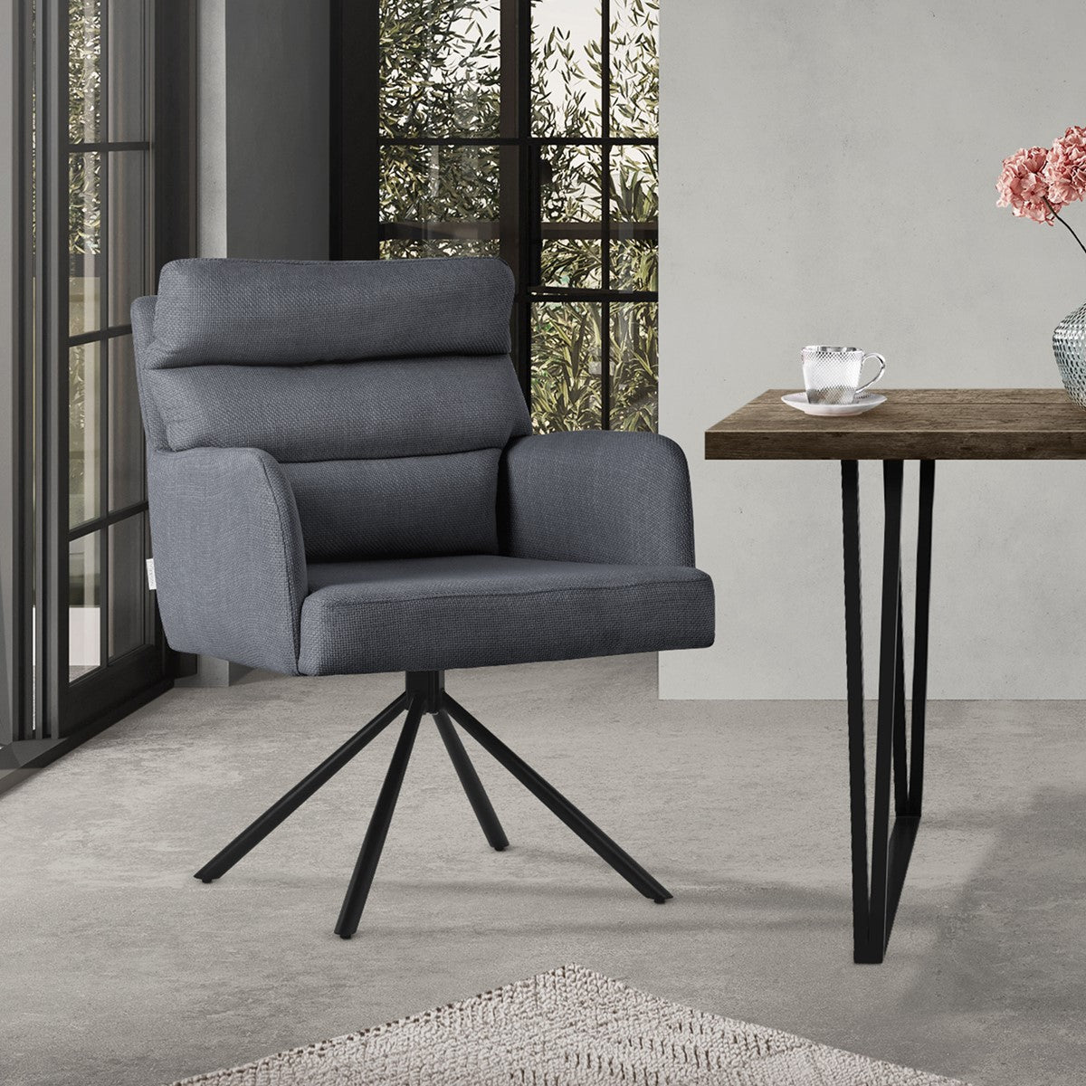 Grey chair next to a table in a room with windows and plants.