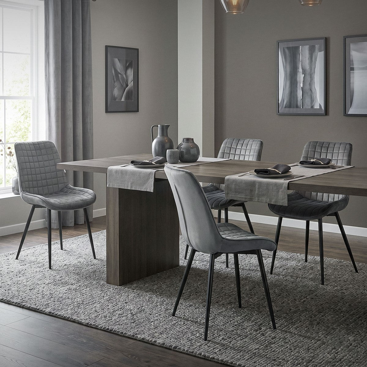 Ein Esszimmer mit einem großen Tisch, grauen Stühlen und dekorativen Bildern an der Wand.