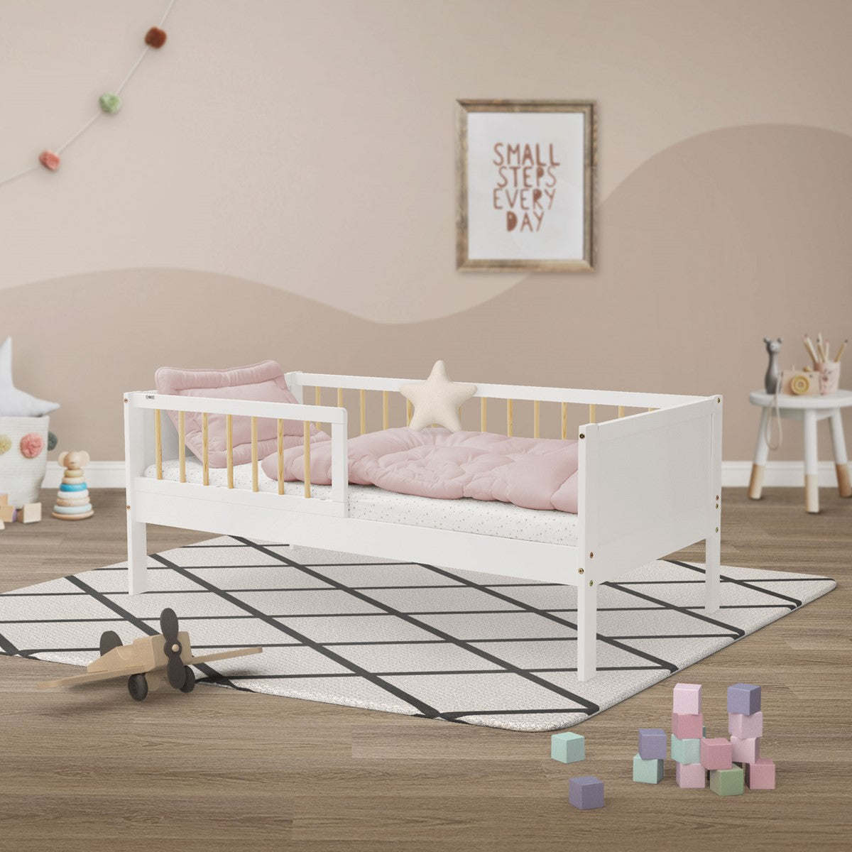 Niedriges weißes Kinderbett mit gelben Gitterstäben, rosa Bettwäsche und sternförmigem Kissen.