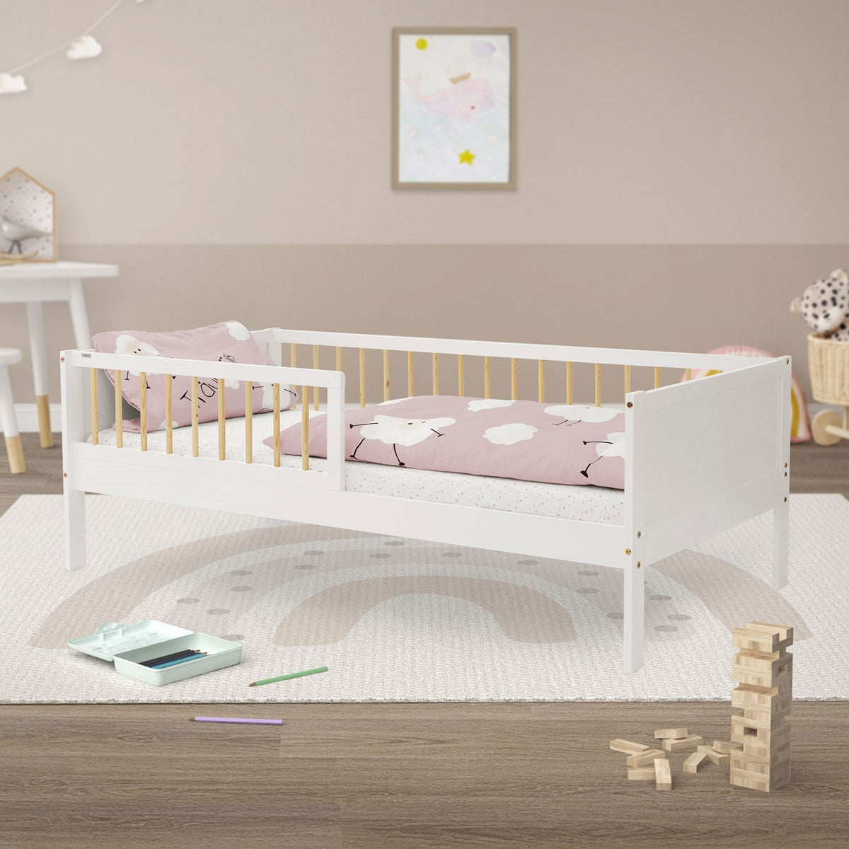 Ein weißes Kinderbett mit rosa Kissen und Spielzeug auf einem Teppich.