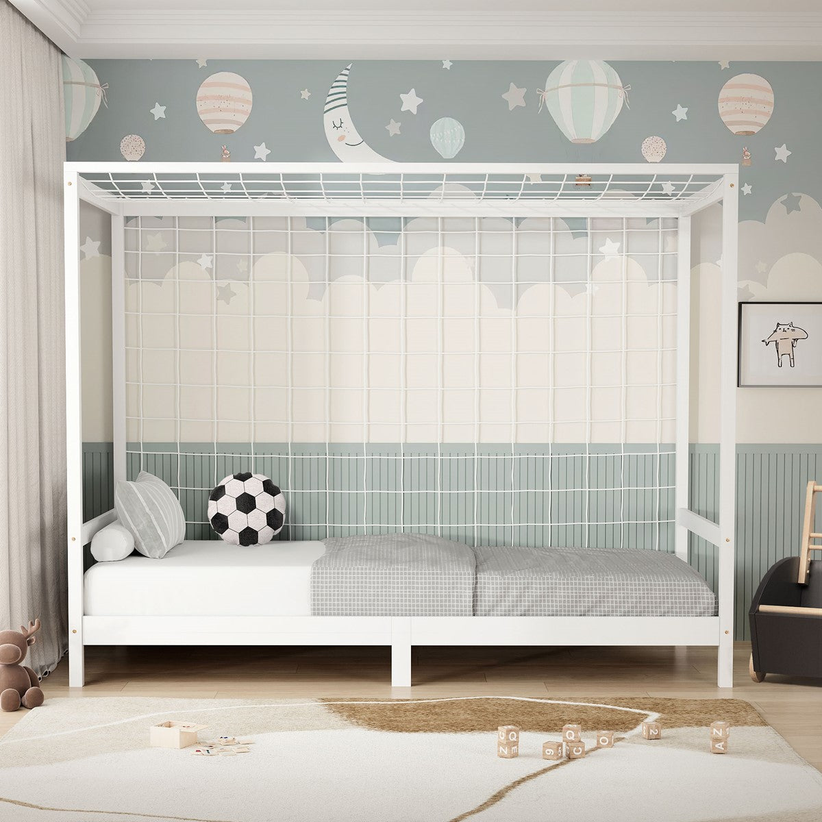 Wit kinderbed met een dak met spijlen, een voetbal en grijs beddengoed, voor een muur met wolken, de maan en sterren.