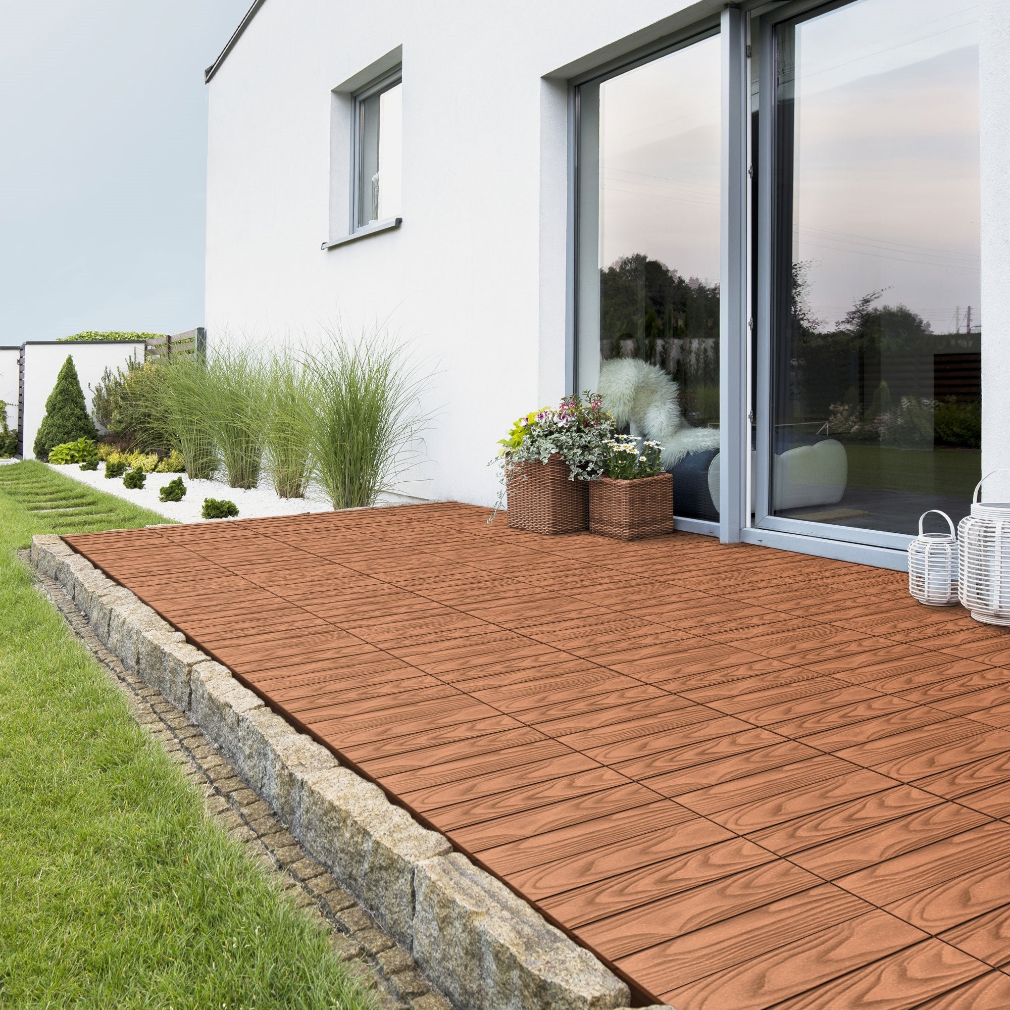 Terrasse mit Fliesen, Pflanzen und einem modernen Haus.