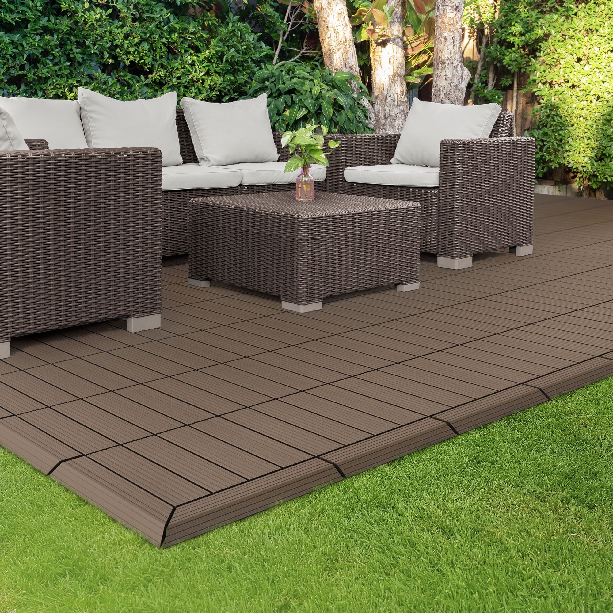 Sitzgruppe aus Rattan auf einer braunen Terrassenfläche im Garten.